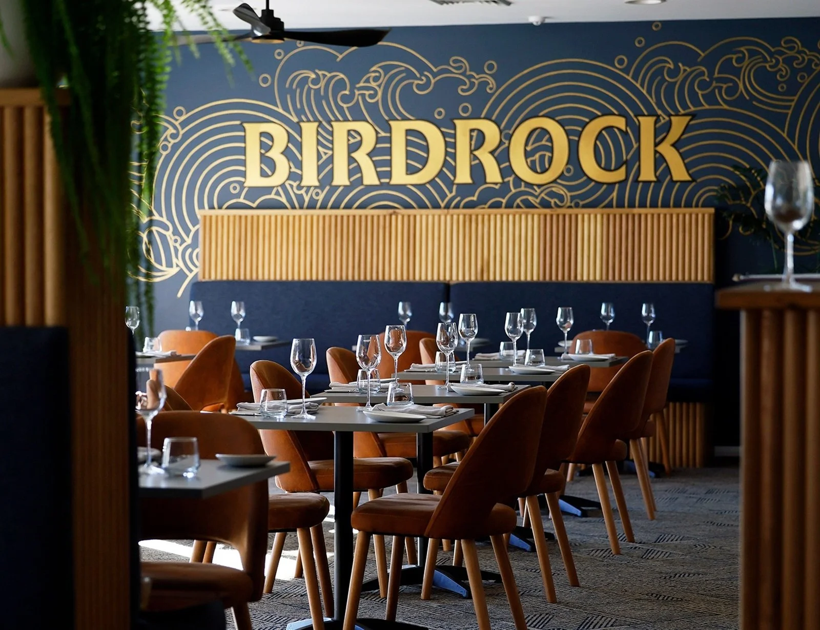 Birdrock Bar & Grill dining room with set tables, warm brown seating, large windows and a Birdrock feature wall.