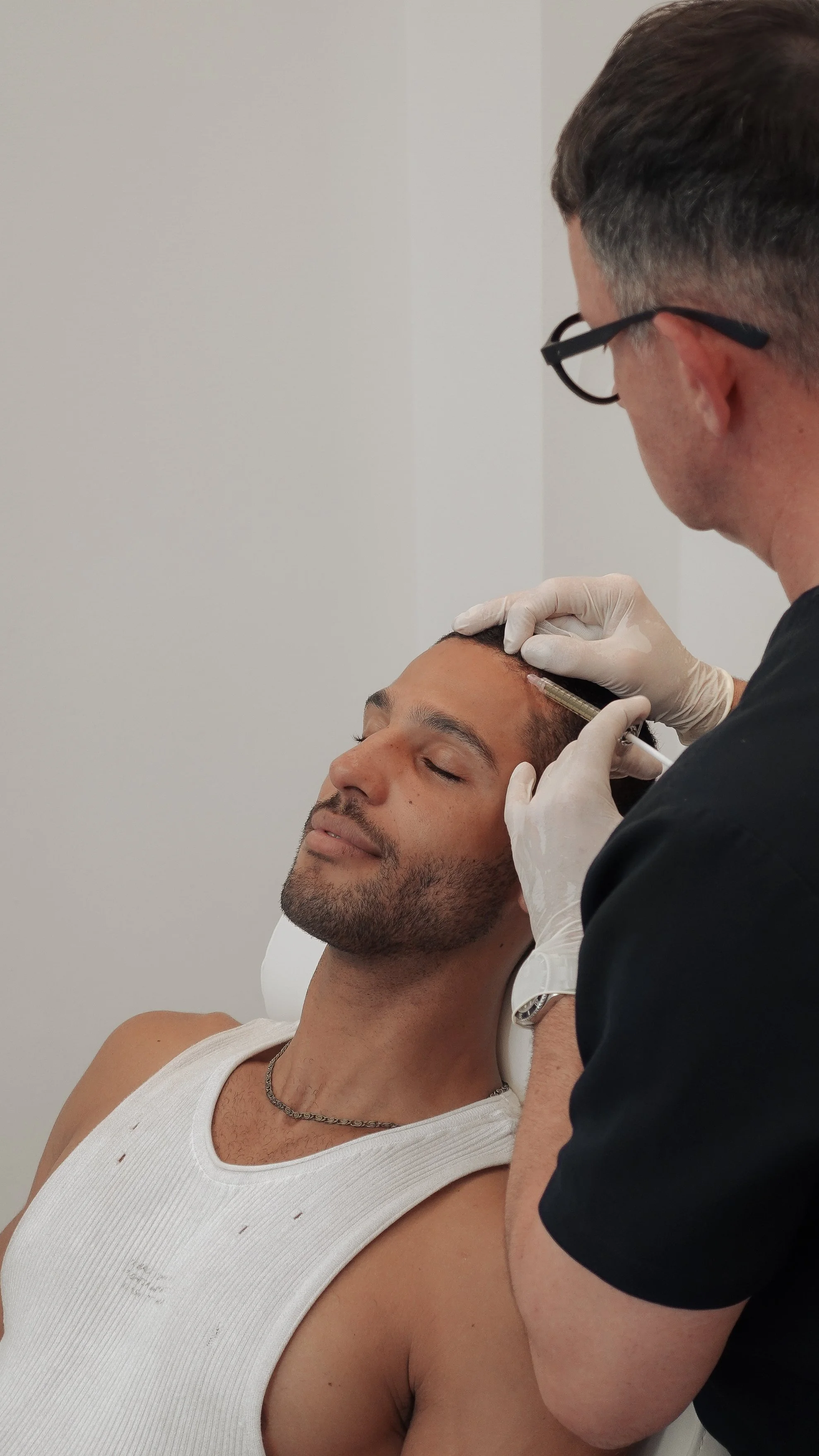 Ein Mann auf einem Behandlungsstuhl. Der behandelnde Arzt injiziert PRP in seine Kopfhaut.