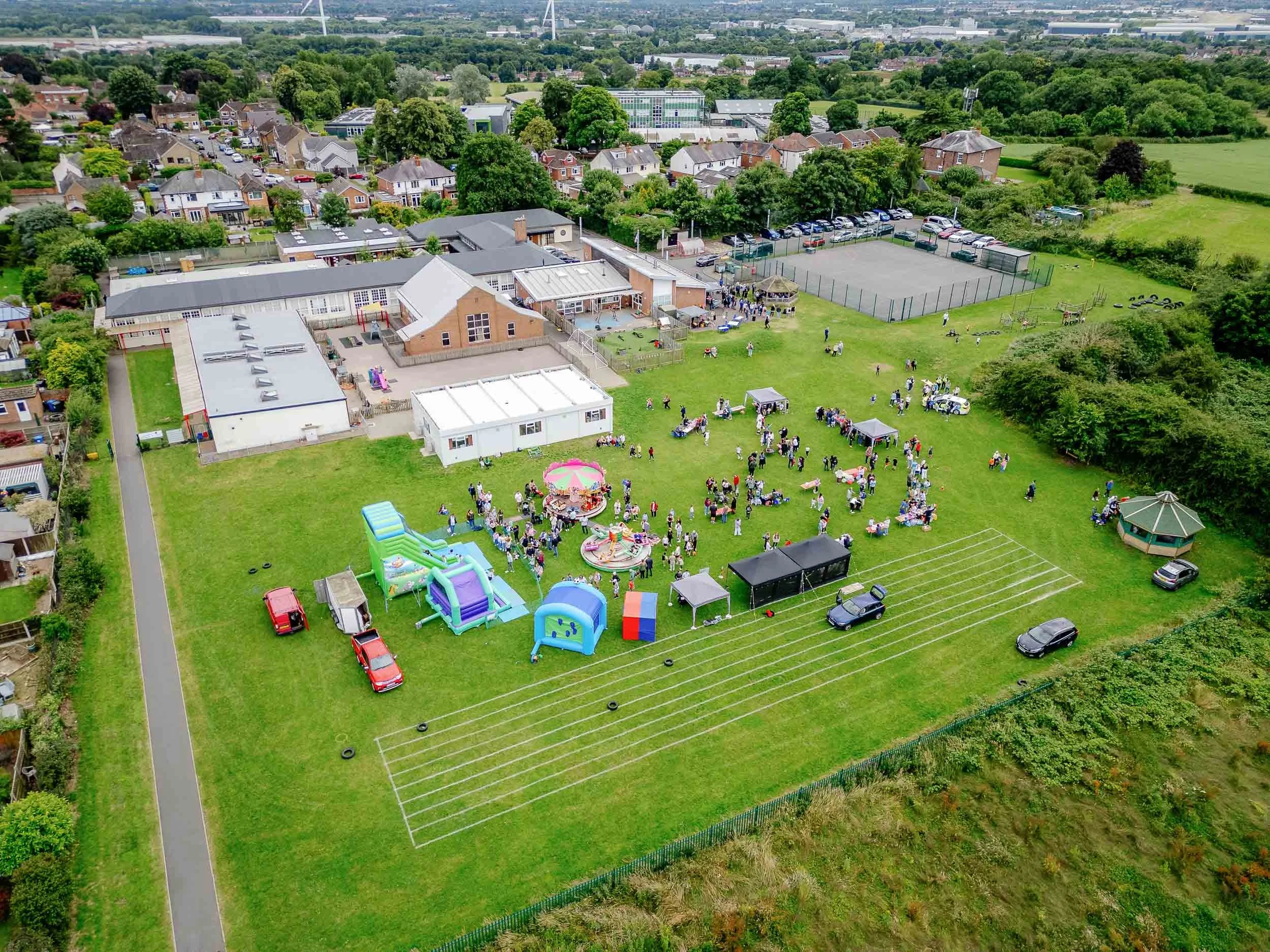 Aerial drone photograph of a school summer fayre featuring colourful rides, stalls, and crowds of people enjoying the event