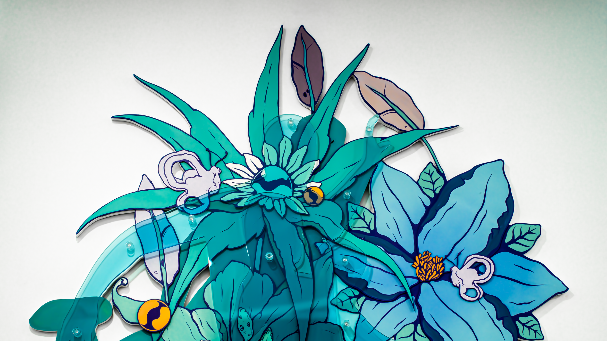 Arte de parede com desenho de flores e folhas em tons de azul, roxo e amarelo, feitas de material translúcido.