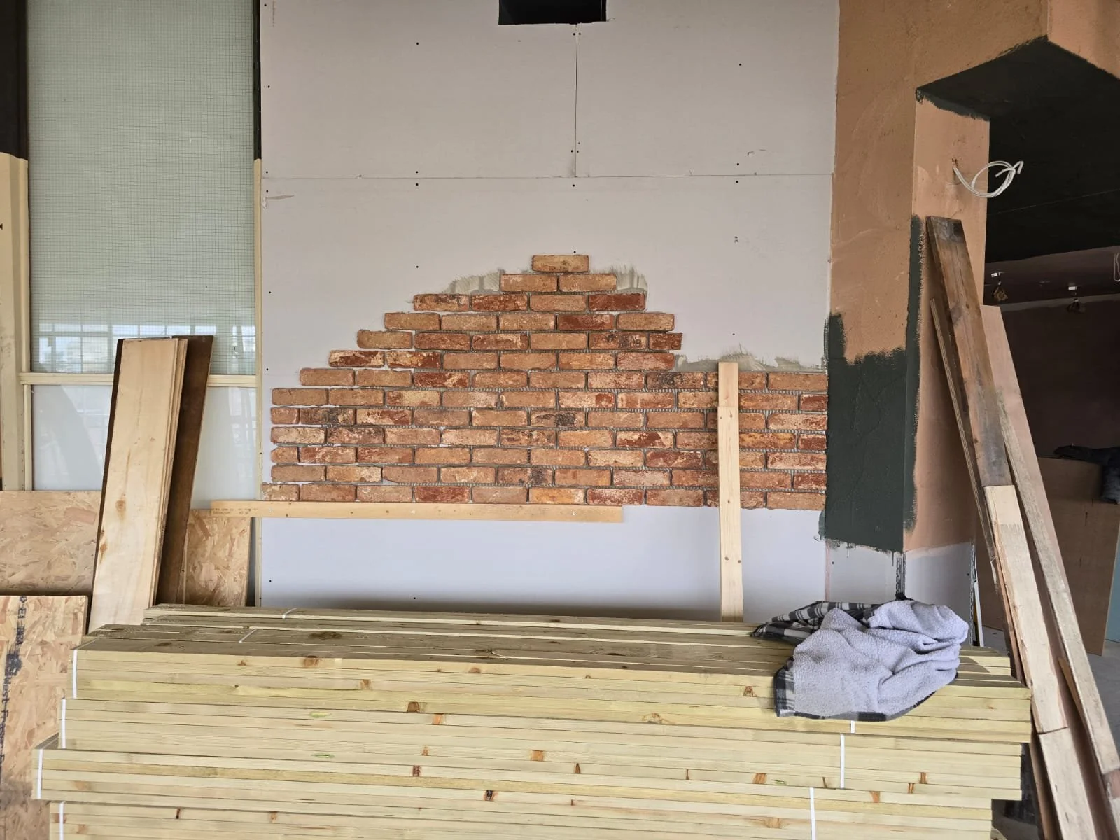 Interior of a construction site with partially built brick wall, wooden planks, and tools.