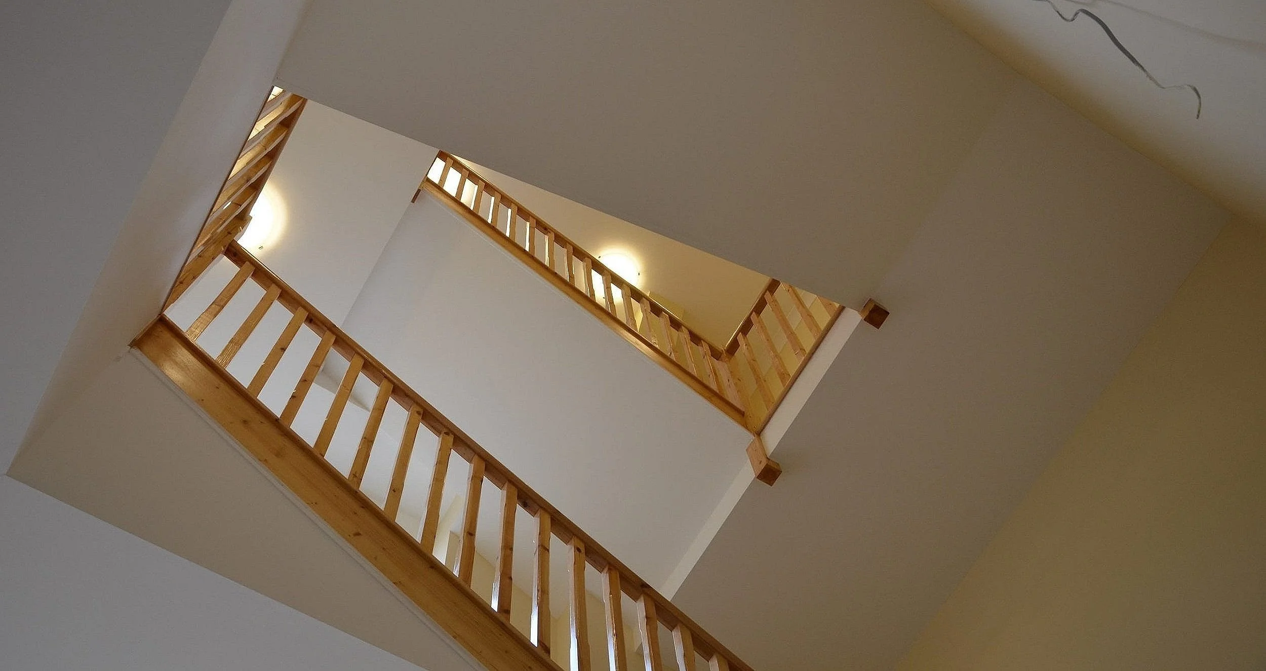 Multiple floors of an indoor staircase viewed from below, with wooden railings and white walls.