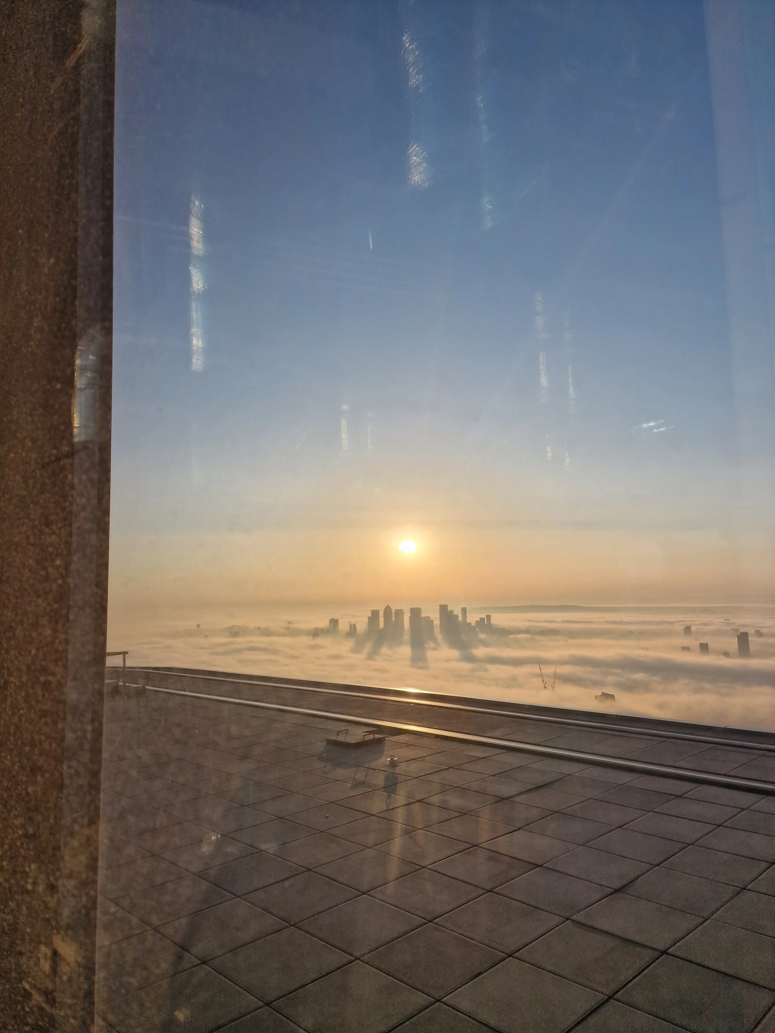 Sunrise over a city skyline with clouds below and reflections on a window.
