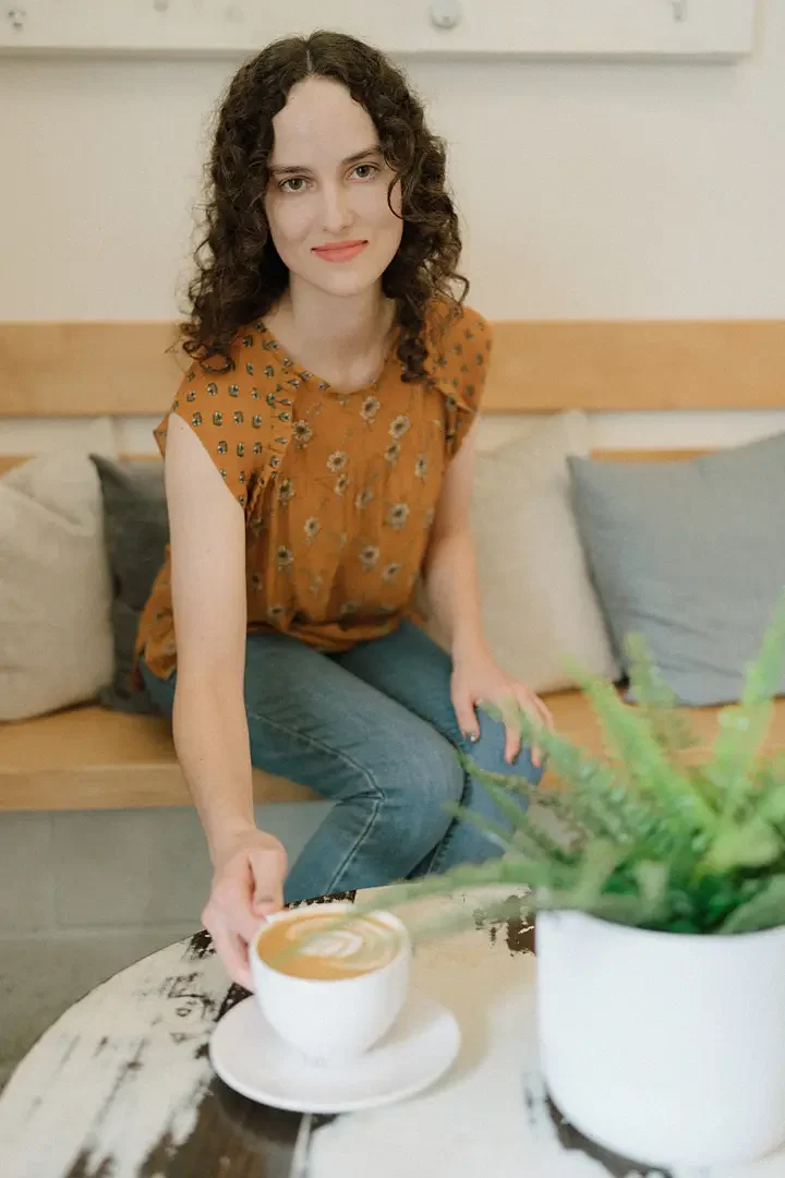 Licensed Therapist, Reagan Hylton, sites on a couch with curly brown hair wearing an orange floral top and blue jeans.