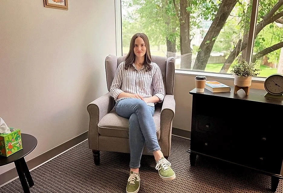 Texas & Colorado EMDR licensed therapist, Reagan Hylton, sits on an arm chair in an office.