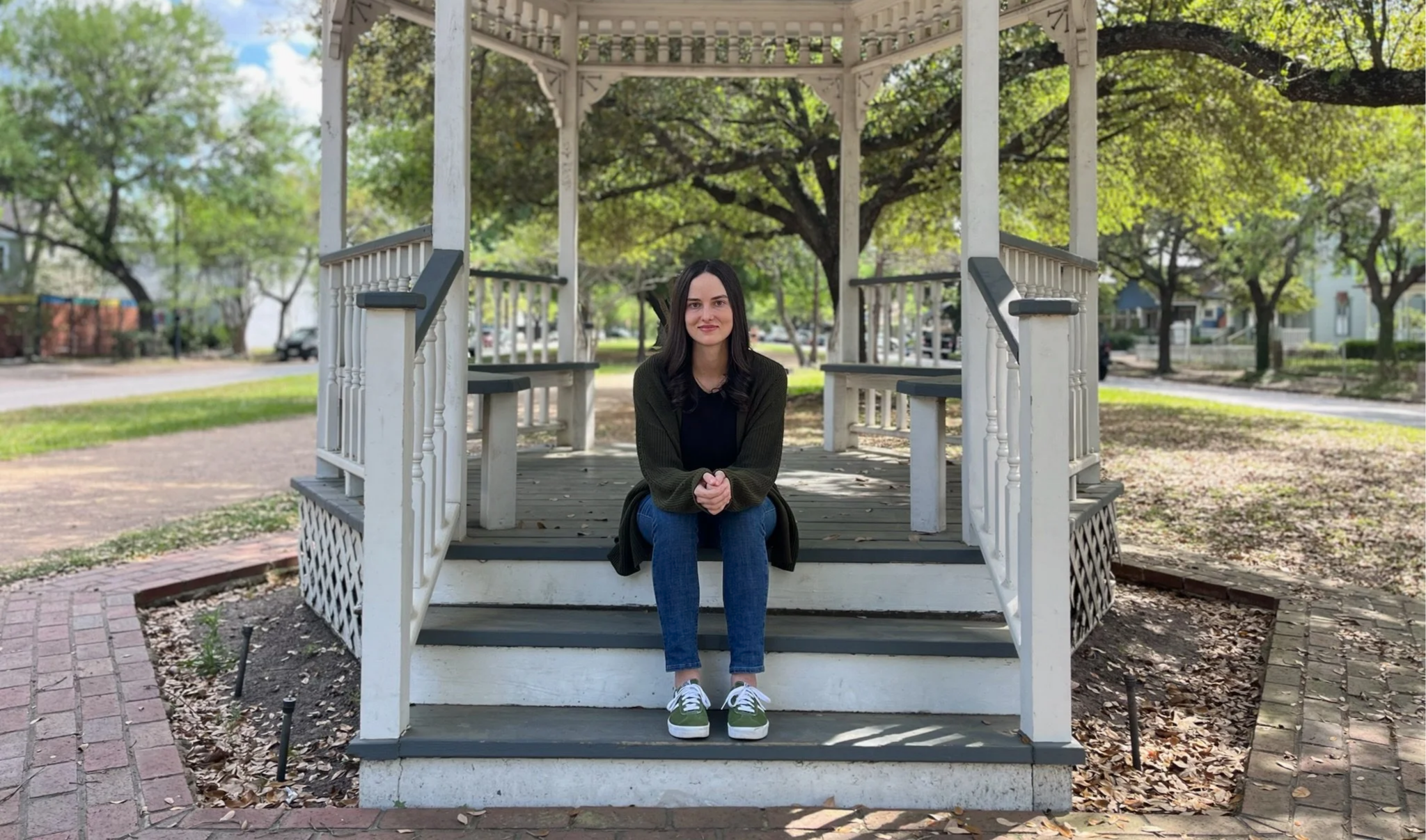 Reagan Hylton, LPC, trauma therapist. Woman sitting on a gazebo with long brown hair wearing a green cardigan