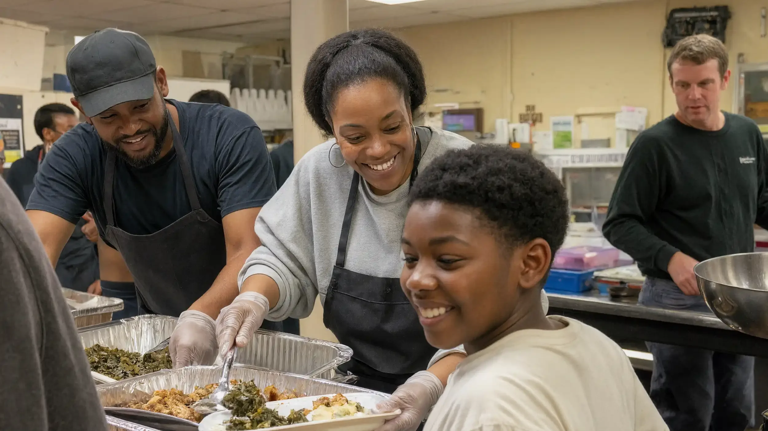 Smiling volunteers serve a hot meal to a young person in a community kitchen