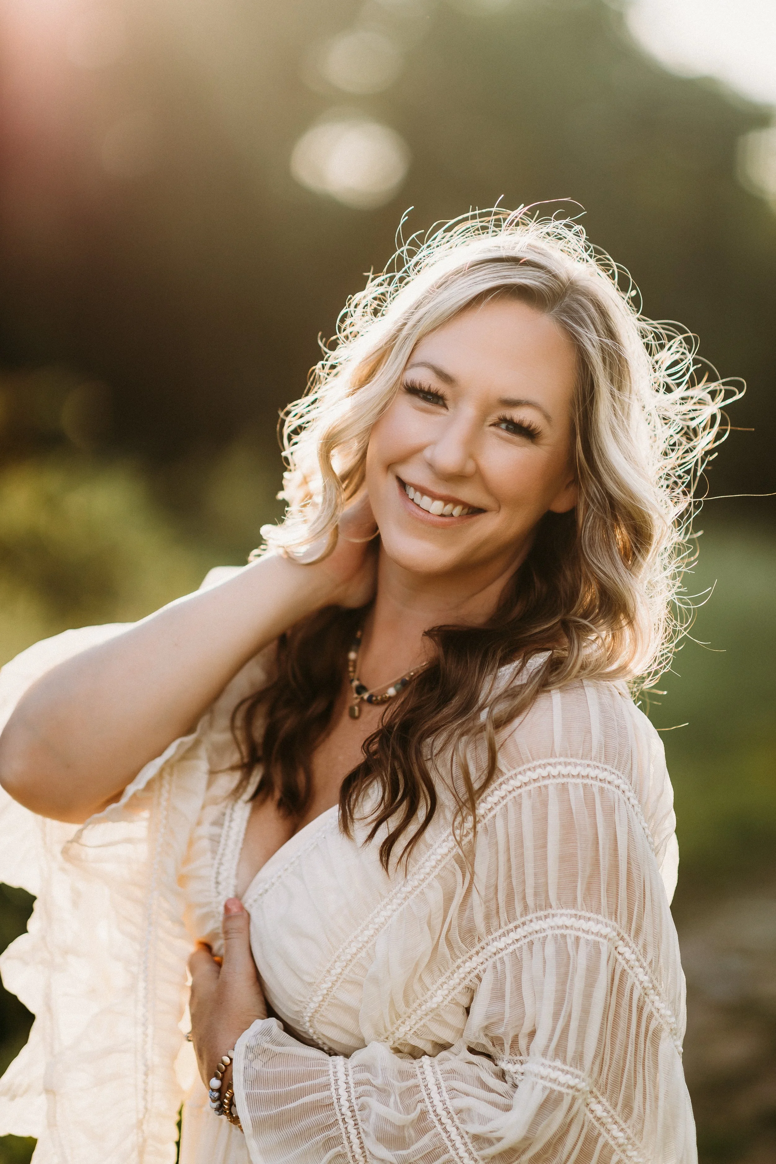 Evie Lynn from Evie Lynn Photography, woman outside with the sunlight shining behind her and she is smiling at the camera.