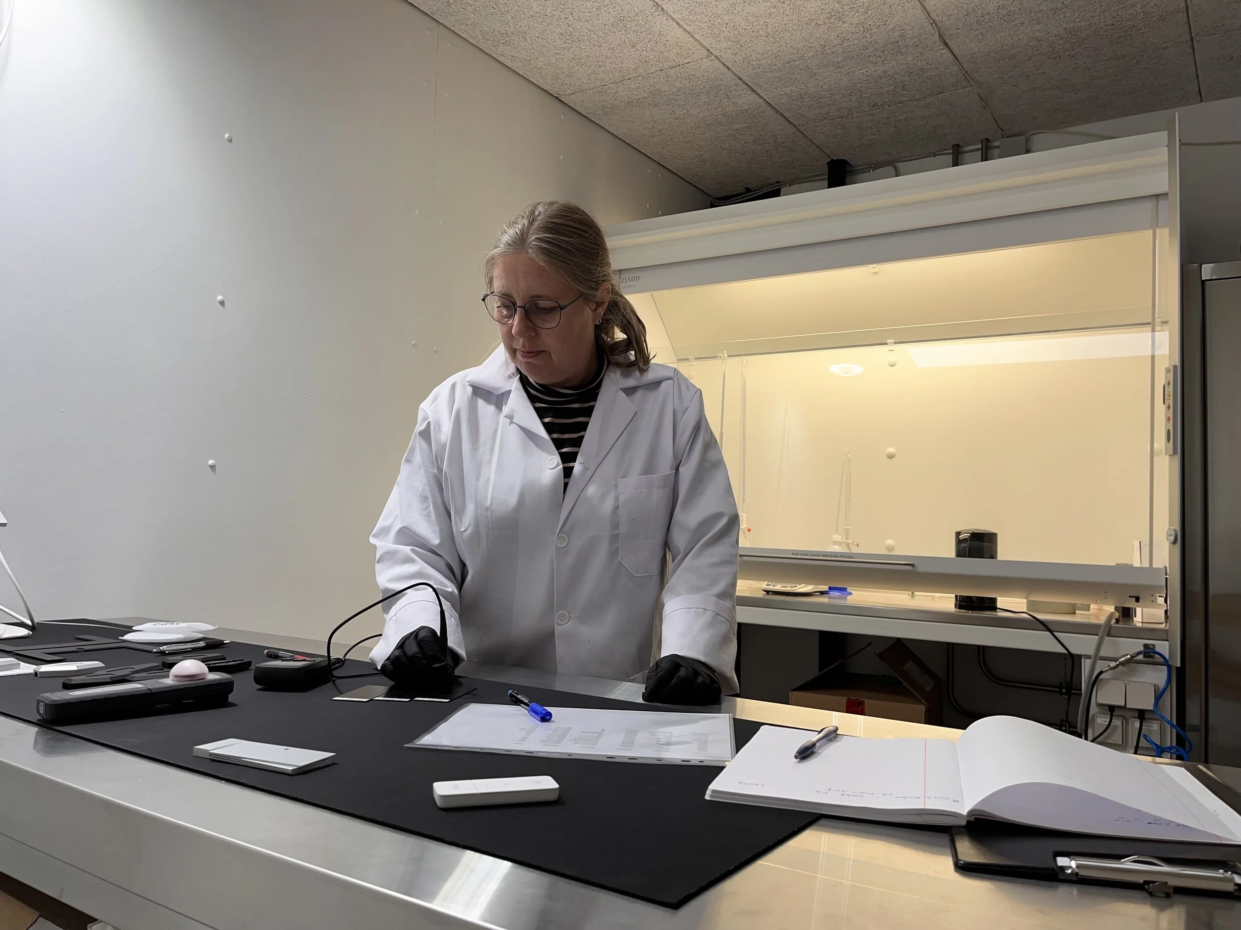 Scientist in a white lab coat and glasses working at a lab bench with scientific equipment and notebooks.