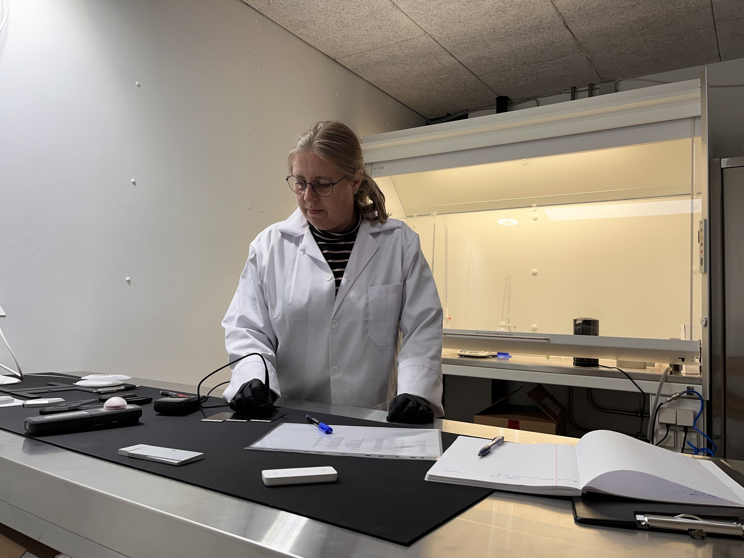 A woman scientist in a white lab coat working at a lab bench with scientific equipment and documents.