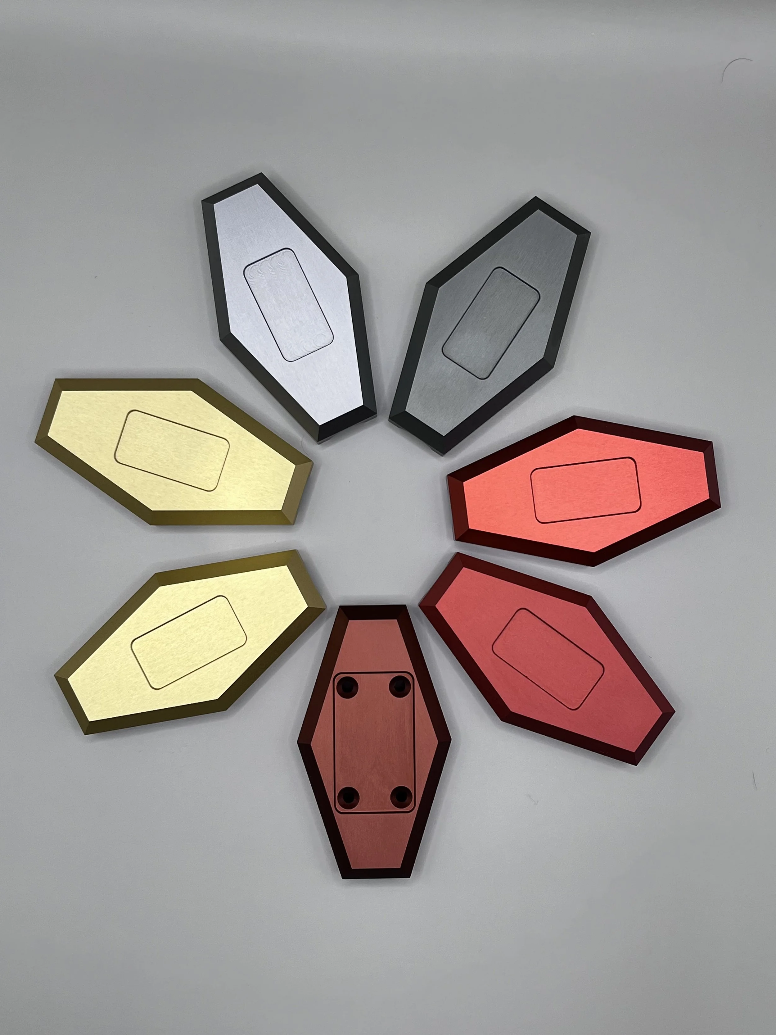 A wall with seven colorful aluminium pieces arranged in a flower shape. The pieces  are in black, gray, yellow, red, and orange, with some illuminated.