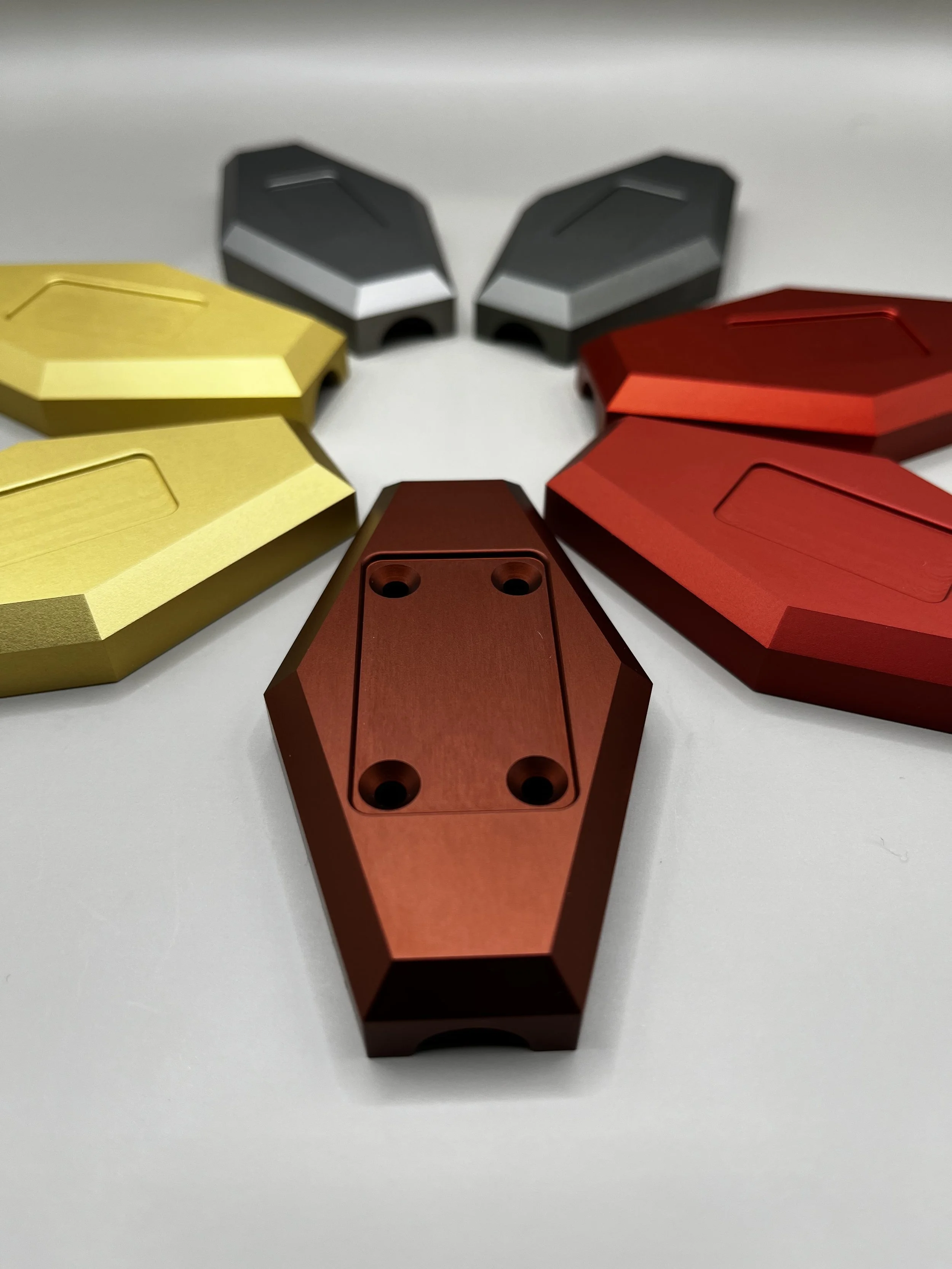 Colorful aluminium objects arranged in a semi-circle on a white surface, with red, gold, and gray pieces.