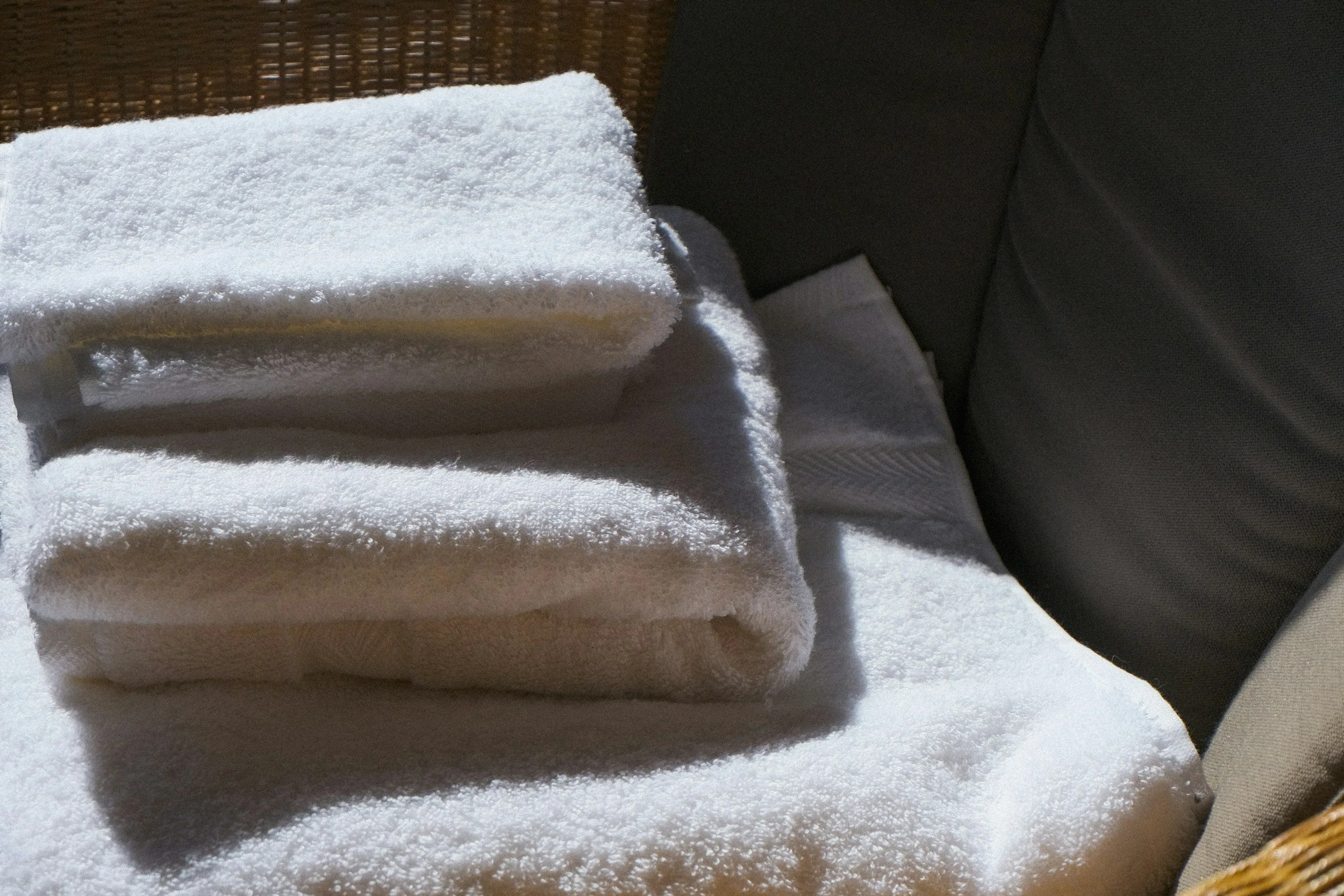 Stacked white towels on a table with a textured dark background and a napkin underneath.
