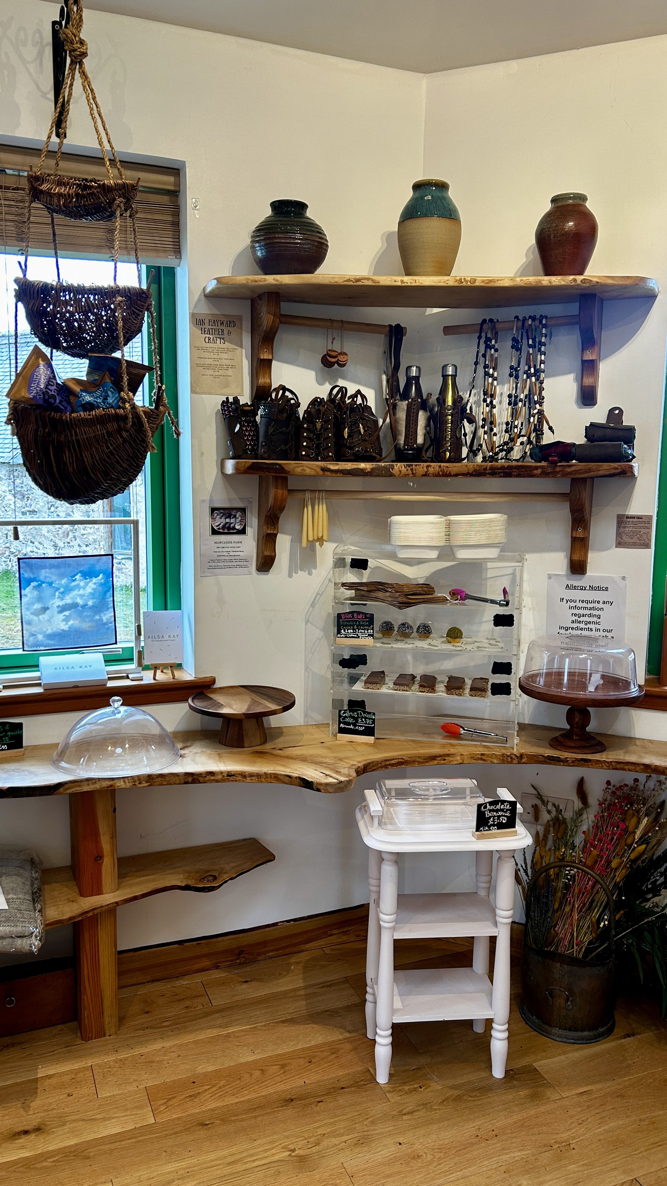 Display of pottery, jewelry, and baked goods inside a boutique shop with wooden shelves and a window.