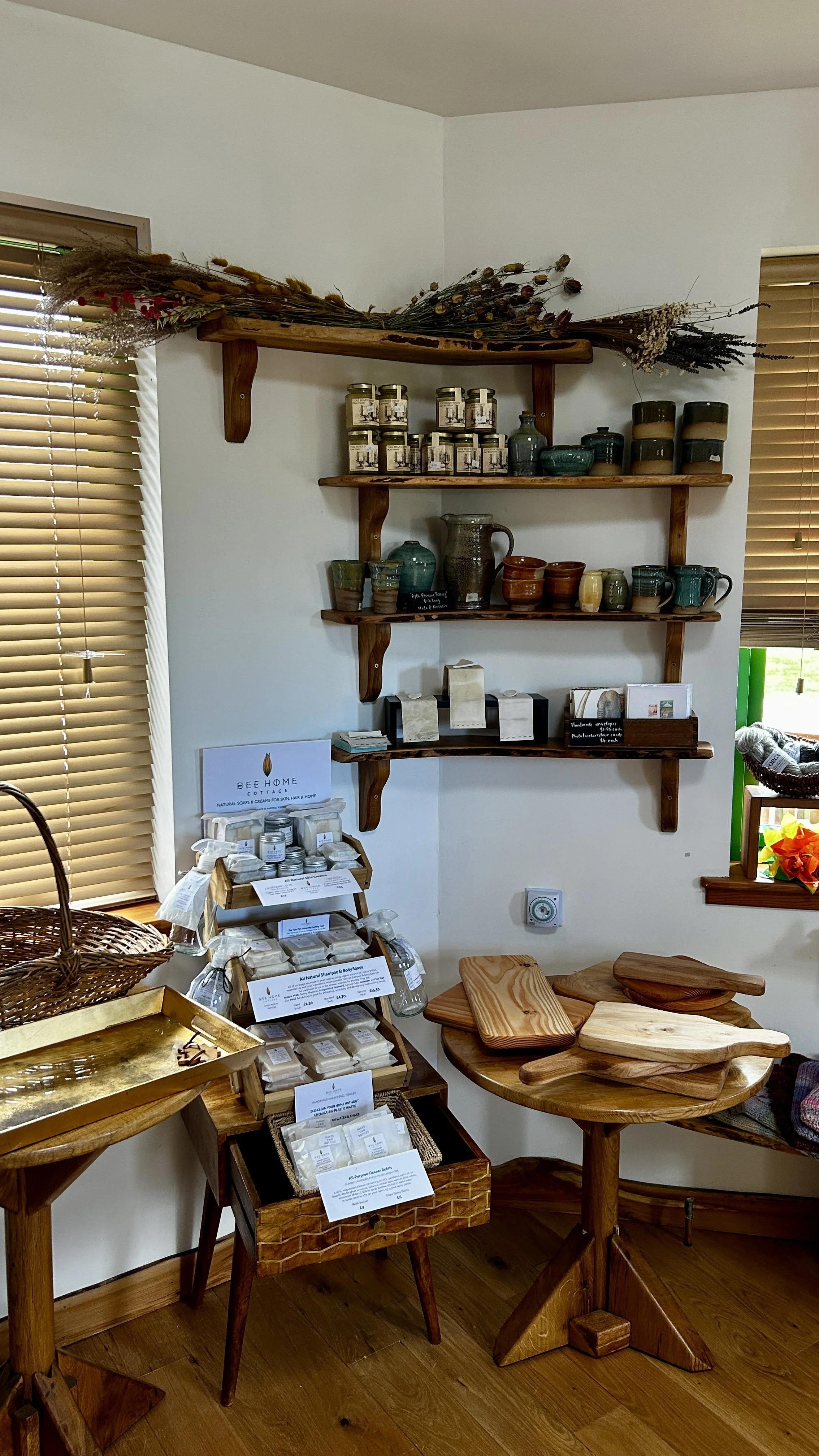 Display of handcrafted soaps, ceramic mugs, and wooden cutting boards in a cozy shop with wooden floors and shelves.