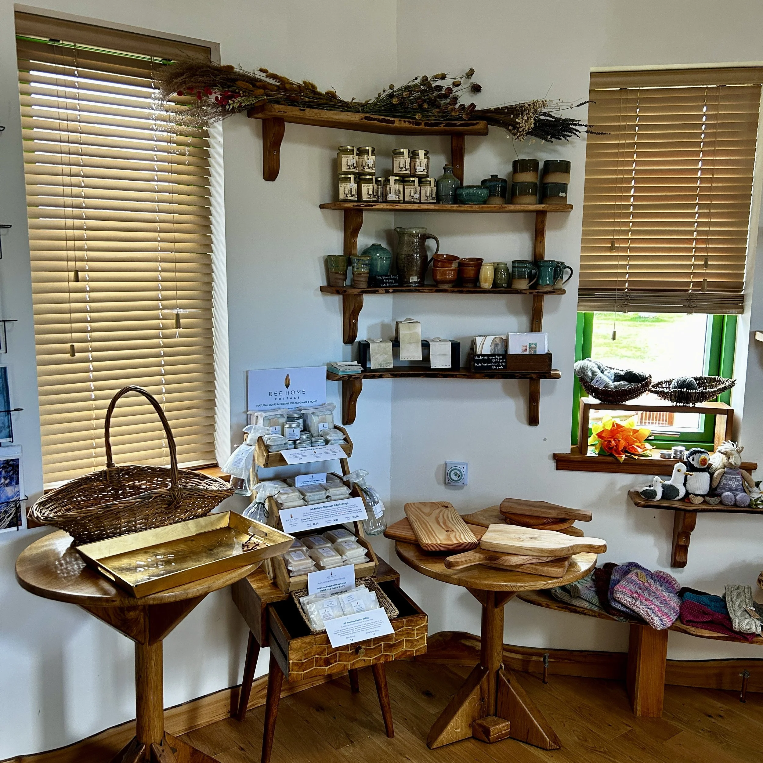 Display of handmade soap, wooden cutting boards, and knitted items in a quaint shop with wooden shelves and window blinds.