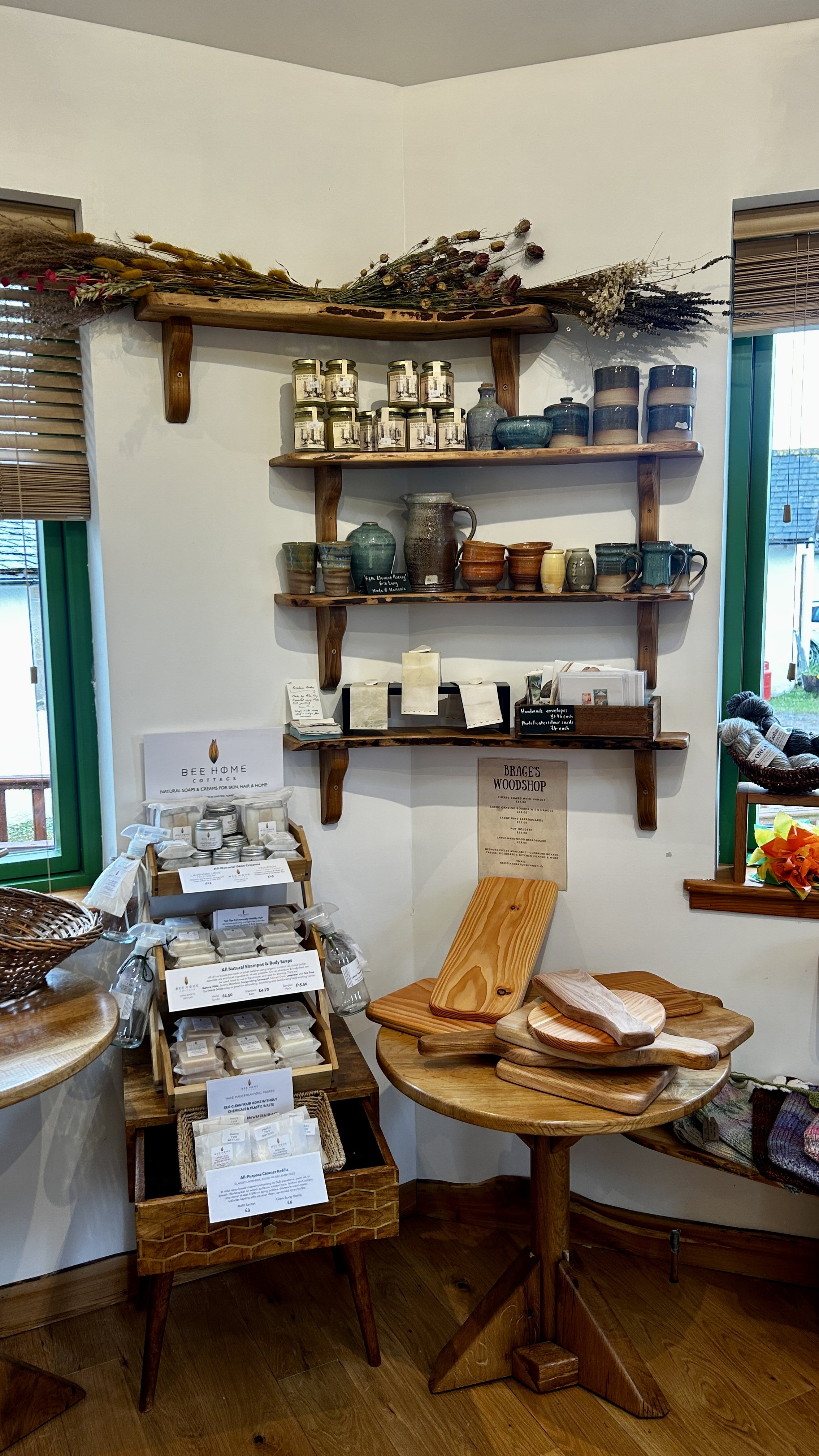 Display of handmade pottery, wooden cutting boards, and natural body products on shelves and tables inside a store.
