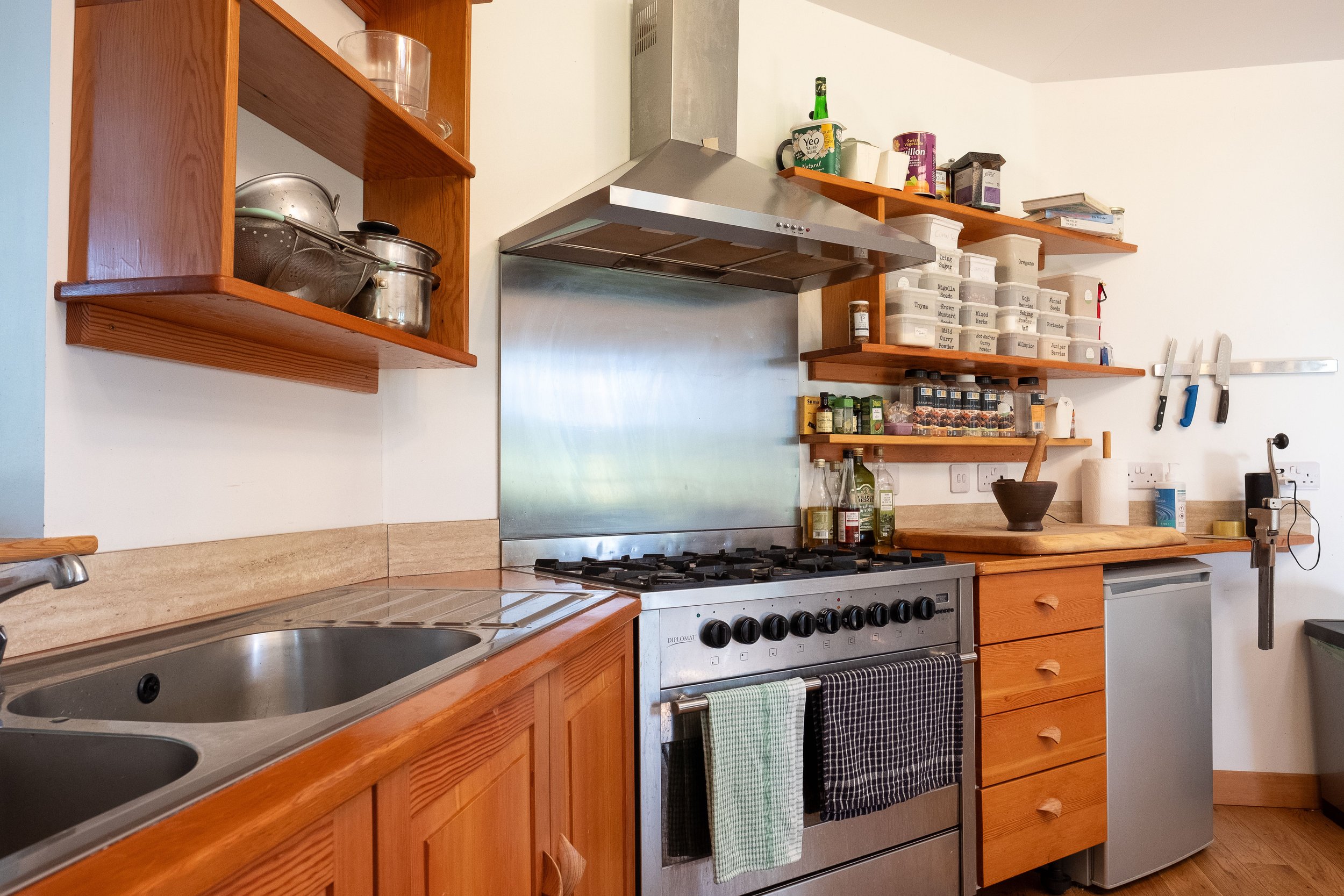 Modern kitchen with wooden shelves, stainless steel stove, metal range hood, and various kitchen items including knives, spice jars, and kitchen utensils.