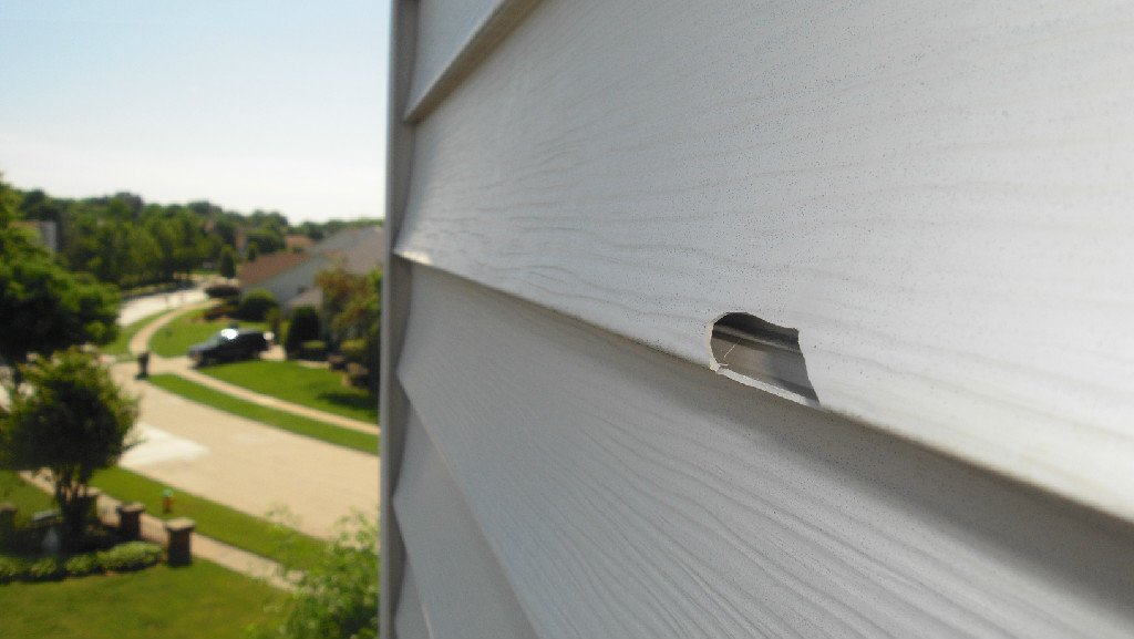 Side of a house with a hole in the siding, revealing the interior.