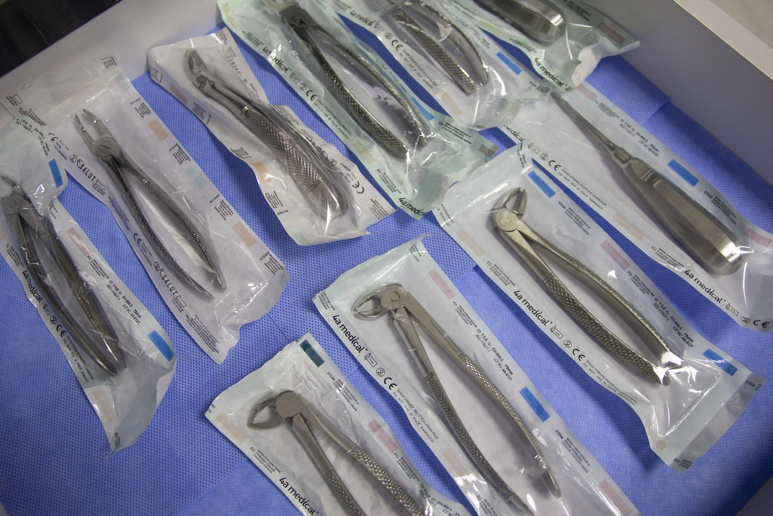 Set di strumenti chirurgici in plastica sterilizzata, confezionati singolarmente, disposti su una superficie blu.