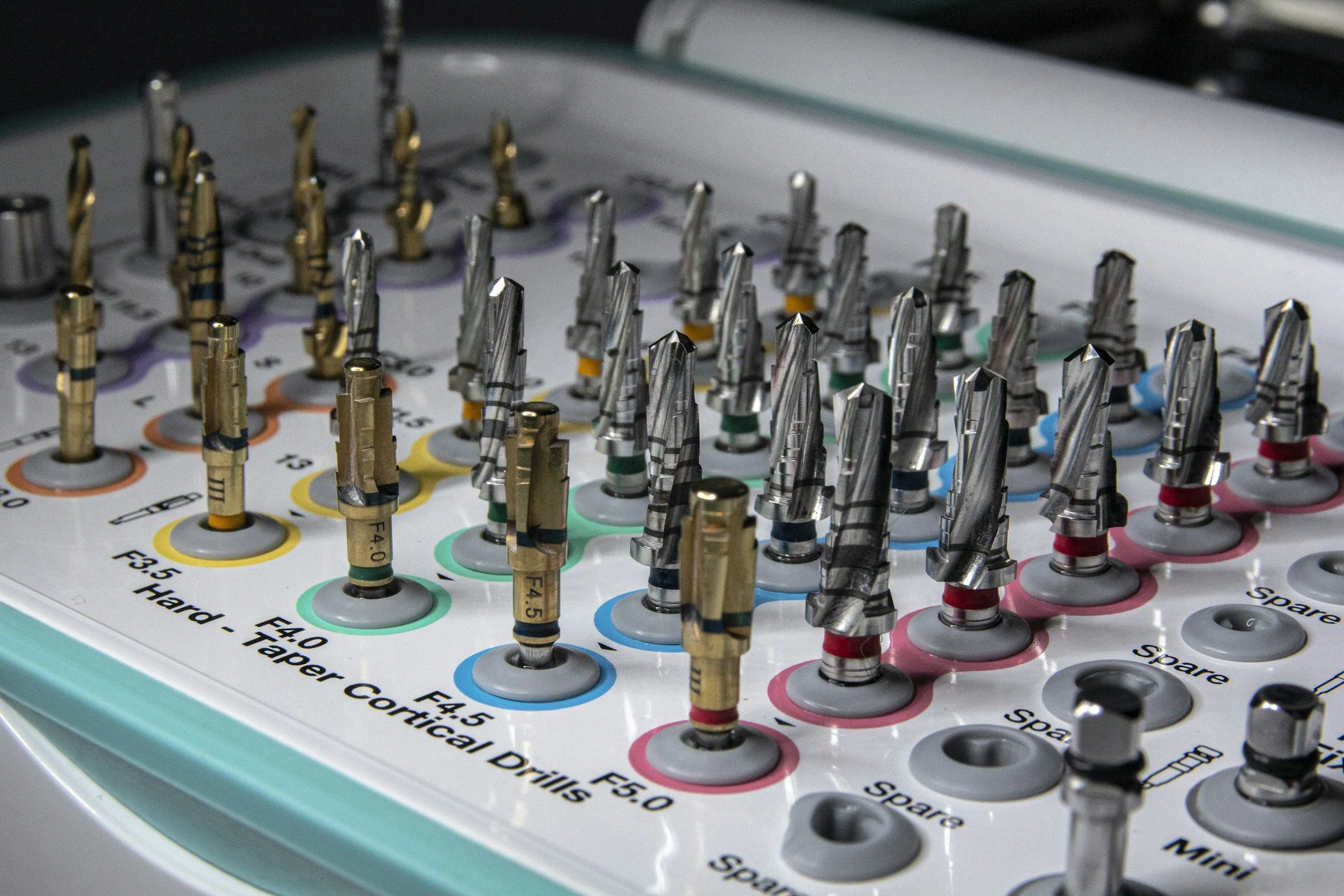 Set di frese chirurgiche di vari tipi e dimensioni su un display con etichette colorate.