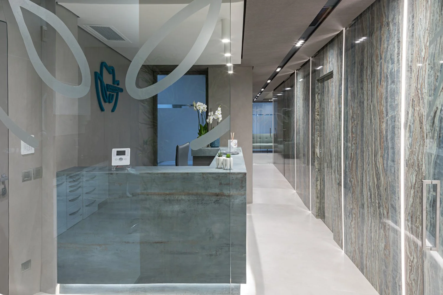 Reception area con pareti in marmo colorato, scrivania in marmo con vasi di orchidee bianche e decorazioni moderne.