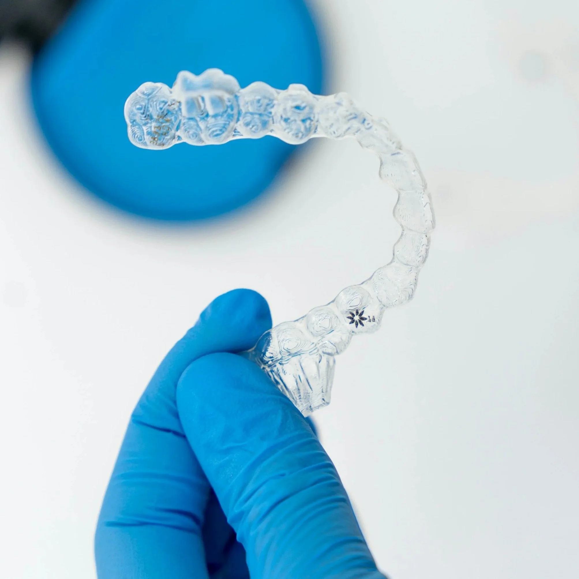 Mano con guanto azzurro che tiene un apparecchio trasparente per l'ortodonzia.