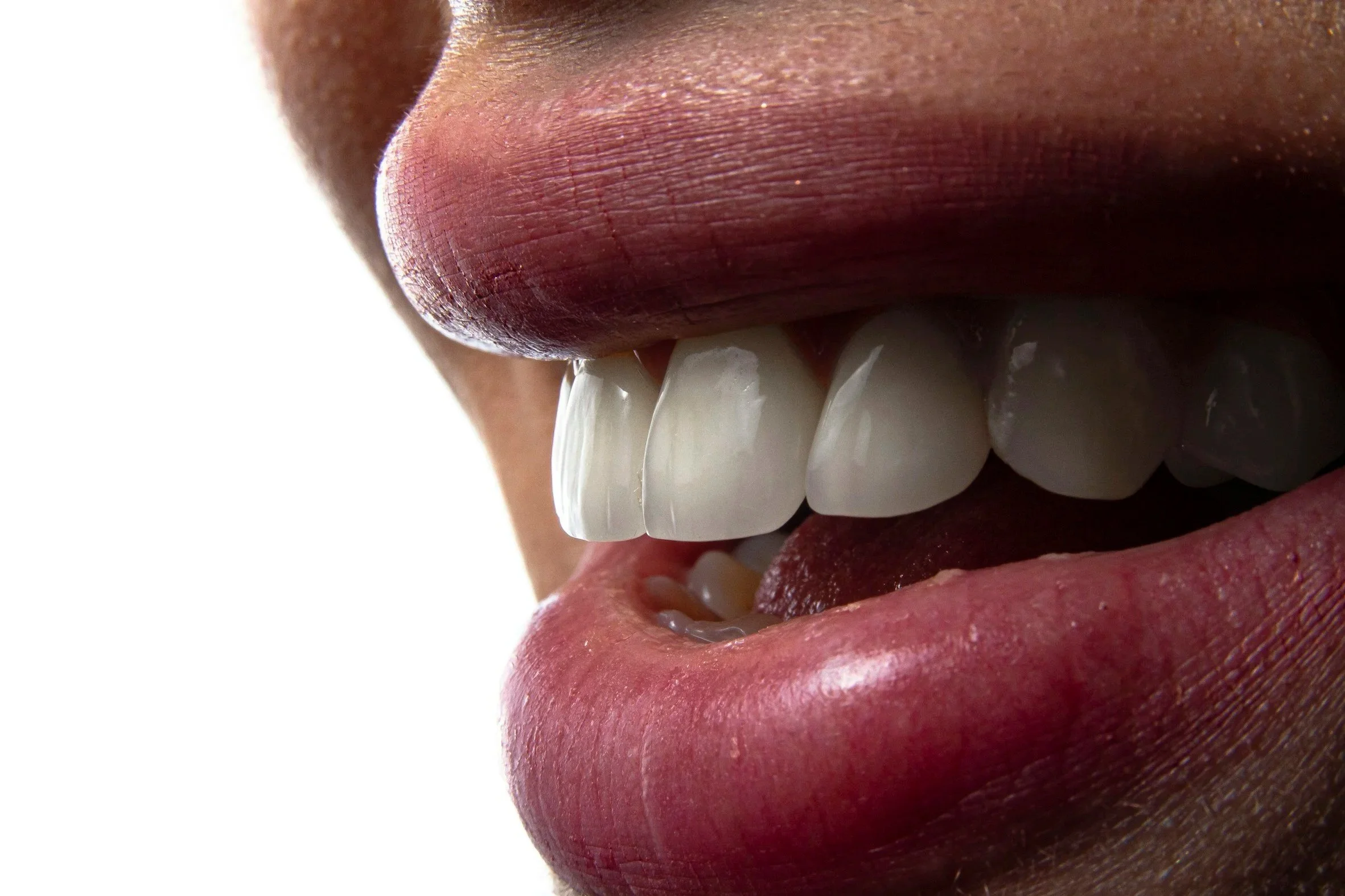 Primo piano di una persona che sorride mostrando i denti bianchi e le labbra aderenti, con la lingua leggermente visibile.