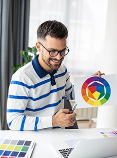 Man wearing glasses and a striped shirt smiling while looking at his phone, holding a color wheel