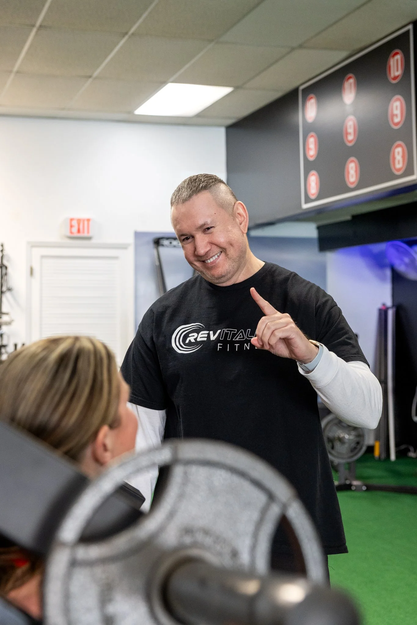 Two men in a gym sitting on exercise bikes, smiling and talking, with gym equipment around them.