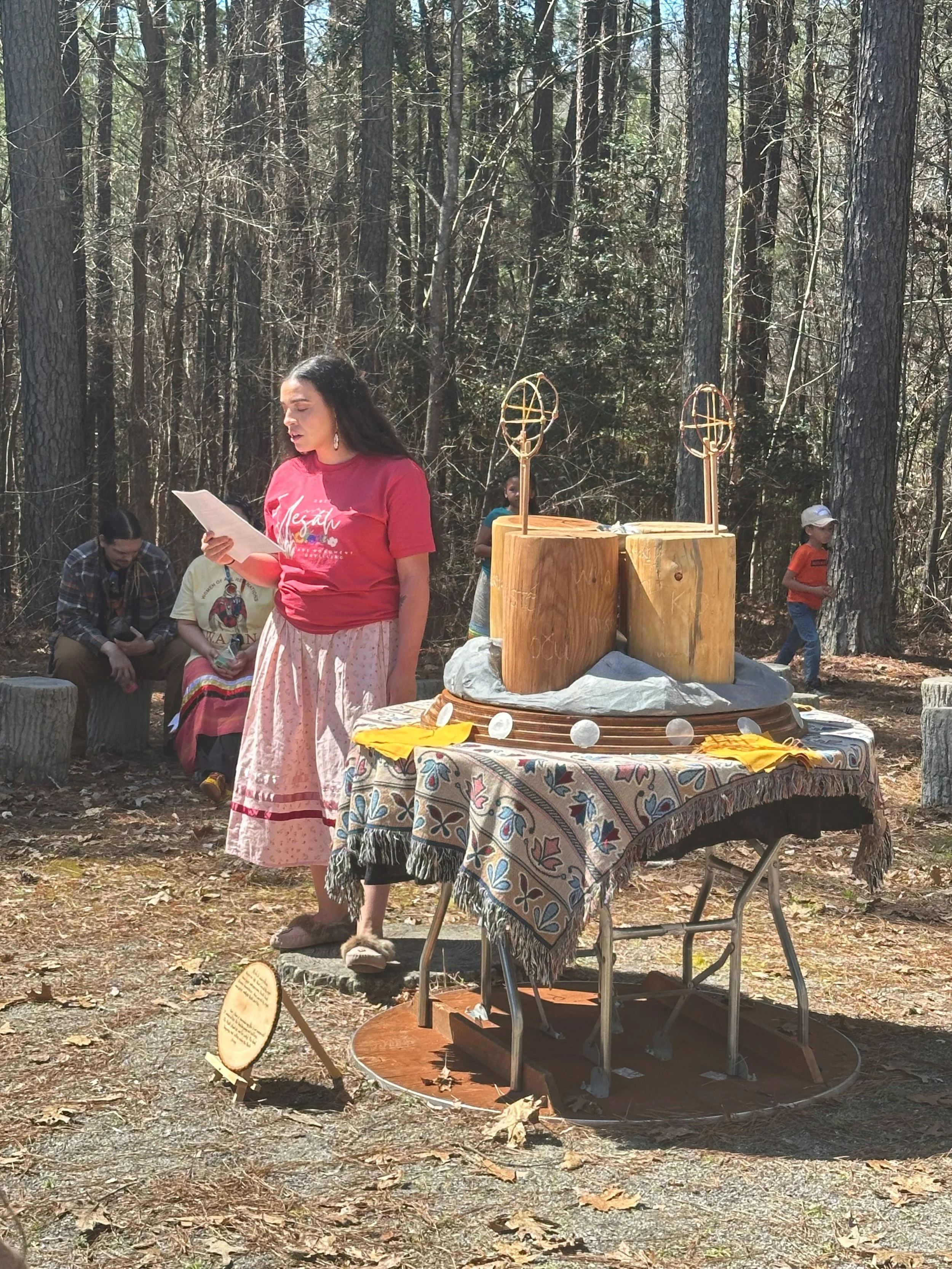 Group of nine people standing outdoors in a wooded area, some holding plaques, during daytime.