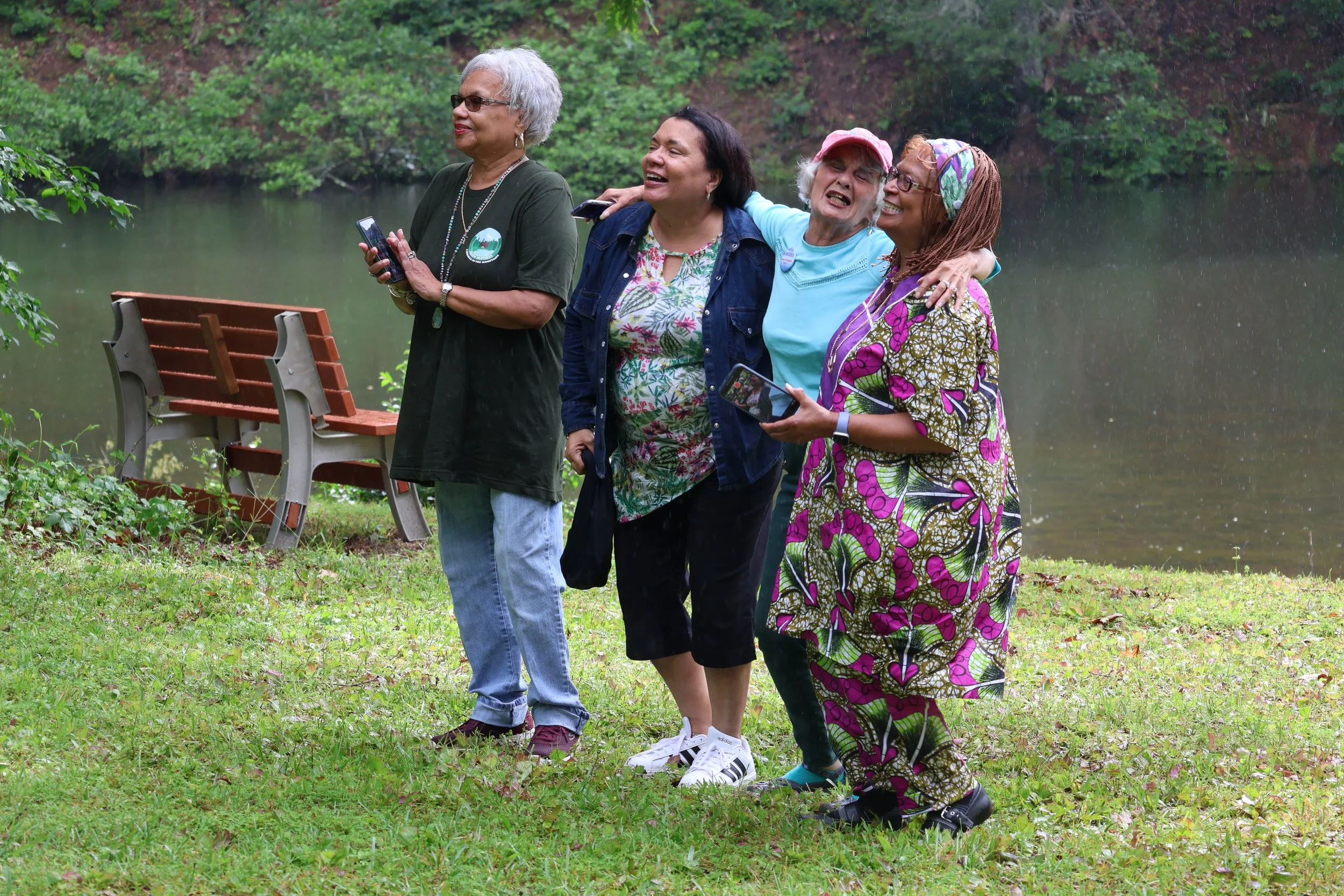A group of people by a lakeside with trees in the background.