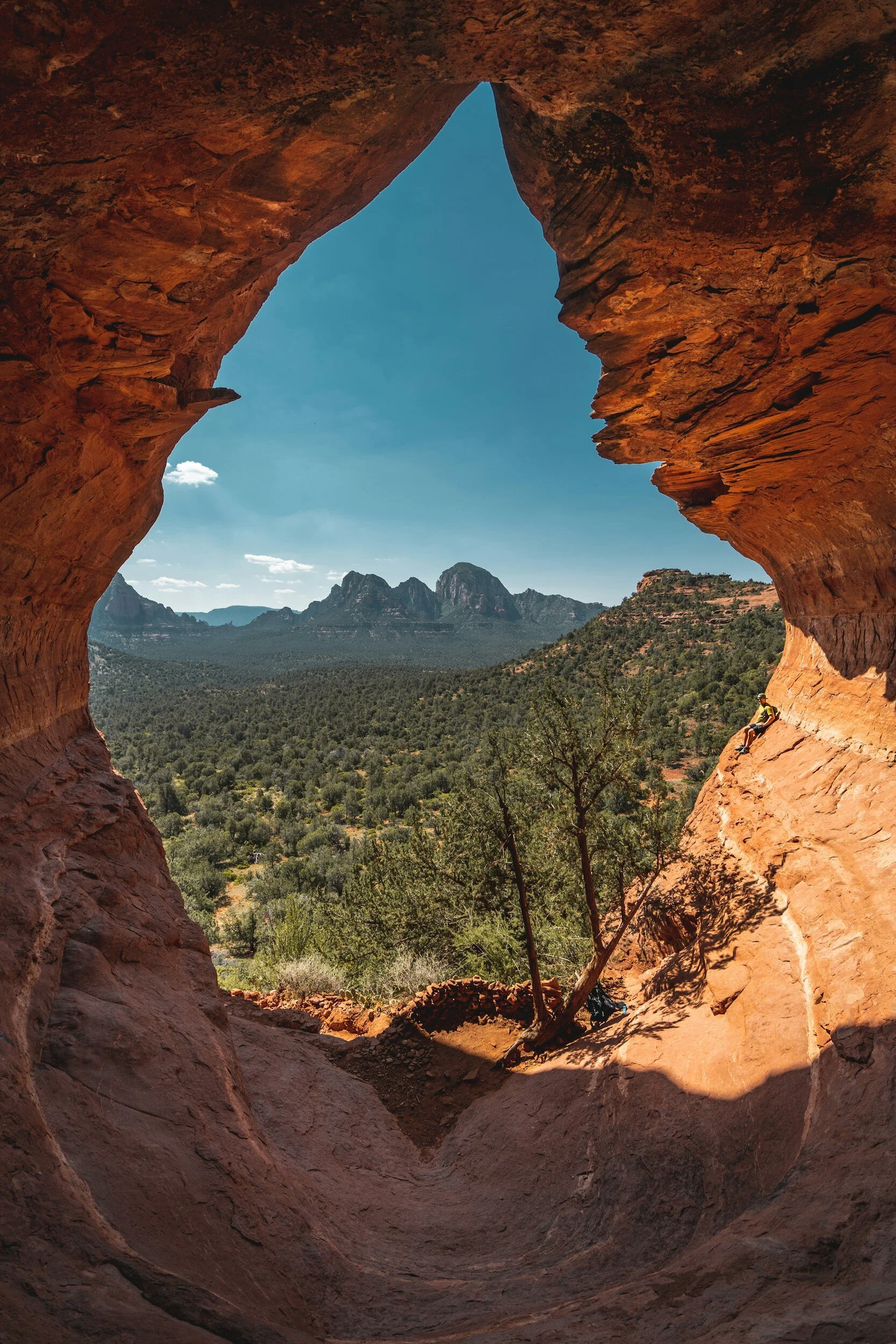 View from inside the birthing cave looking out to a vast landscape of green forest and distant mountains under a clear blue sky.
