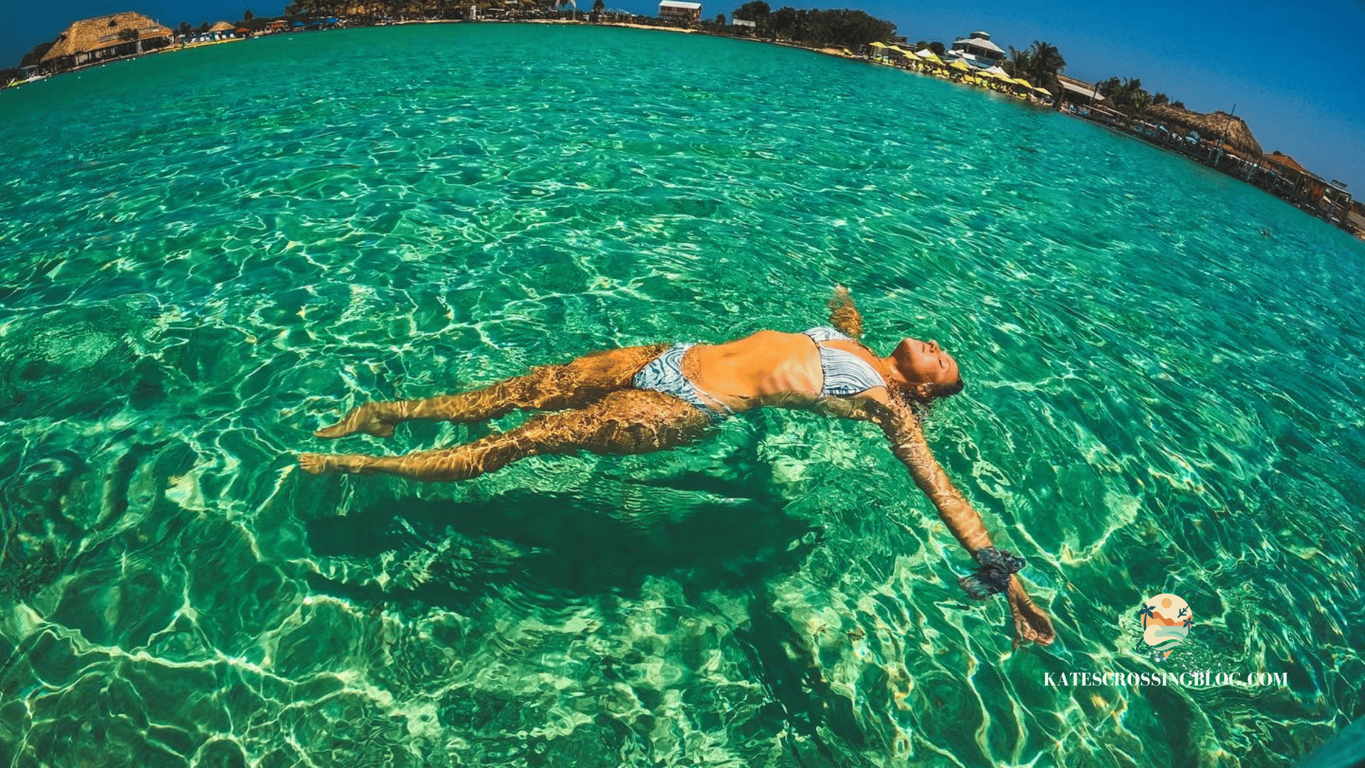 Kate, floating in crystal clear turquoise water with her arm reached out and a secret beach shoreline in the distance. 