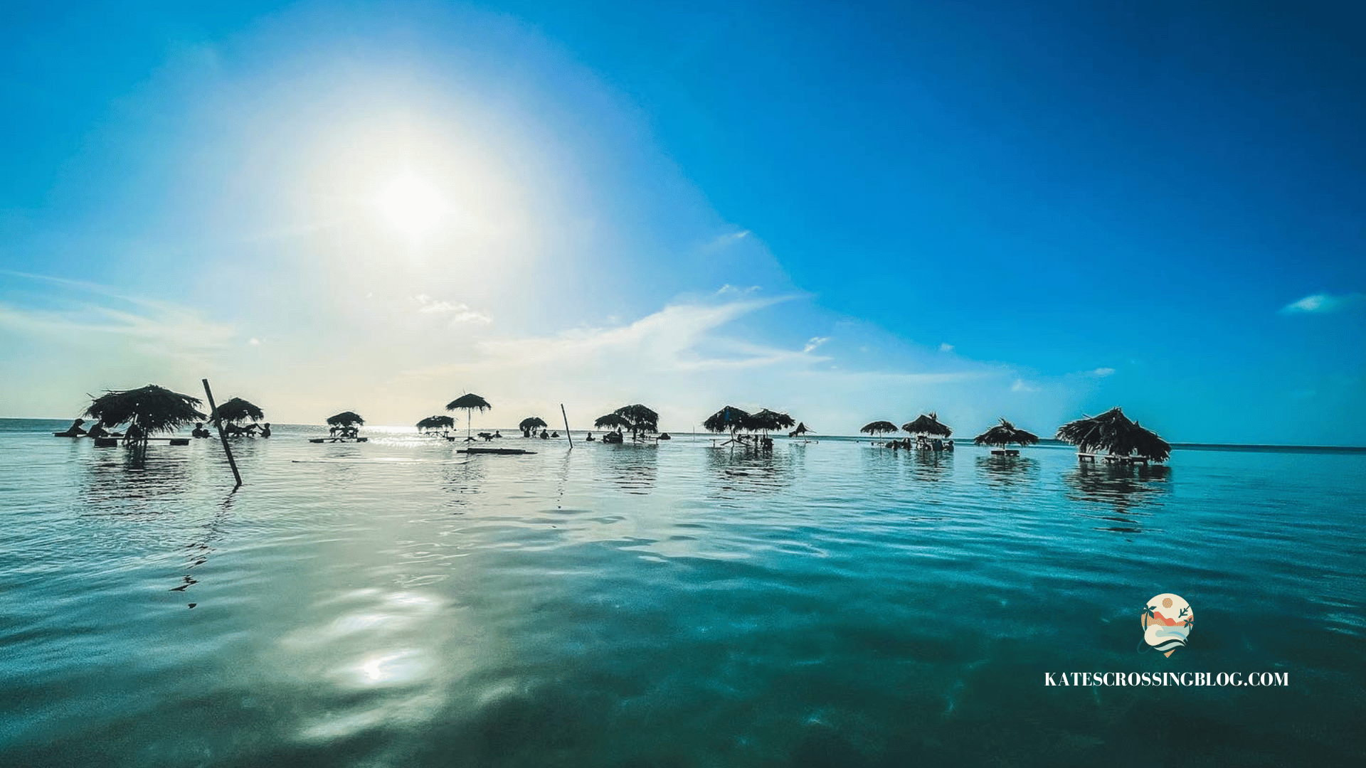 Thatched roof table cabanas out in the turquoise waters of Belize with a sunset in the background. 
