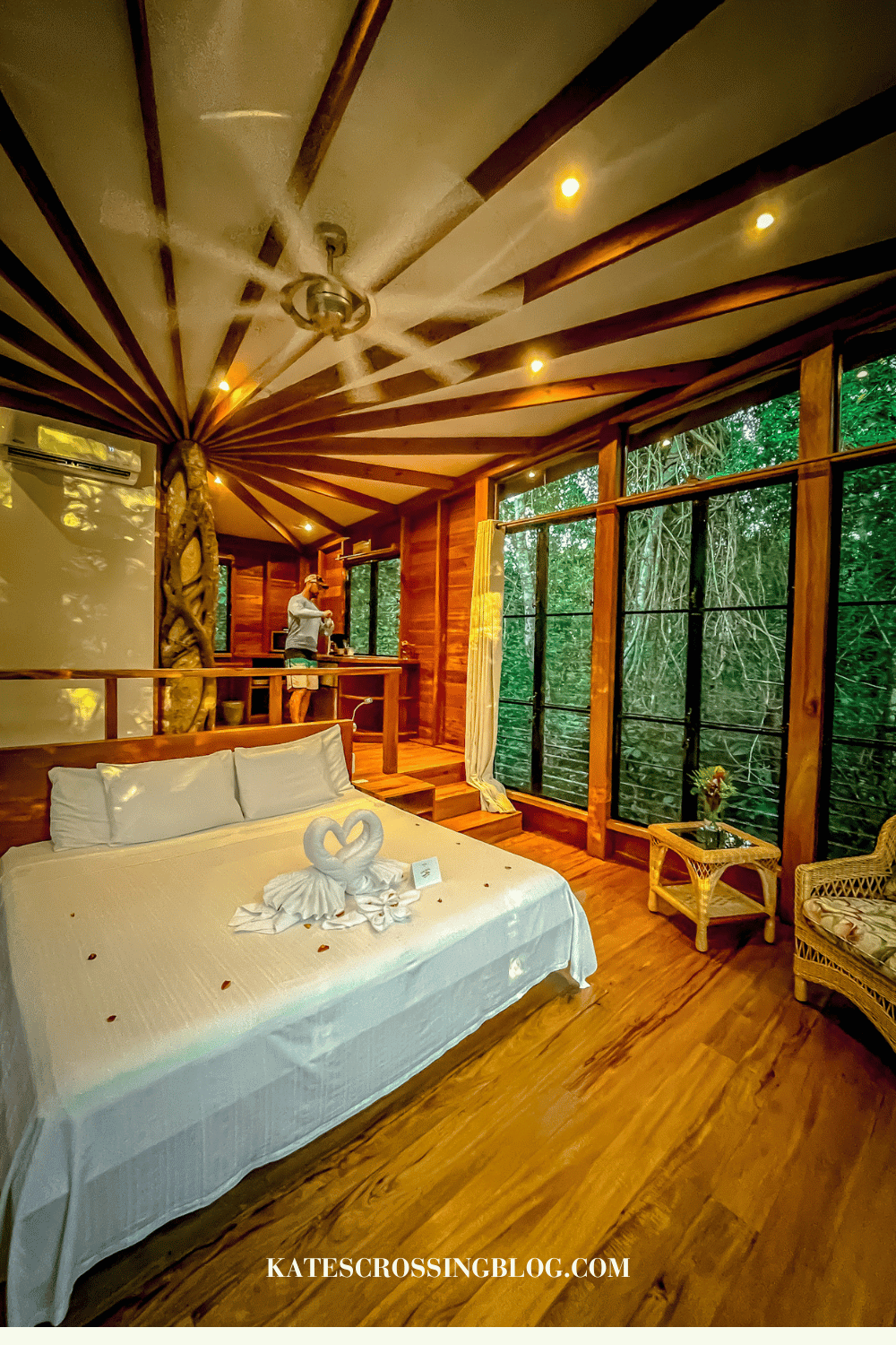 Bed covered with white bedding and two towels shaped like swans and rose petals on the bed inside the tree house.