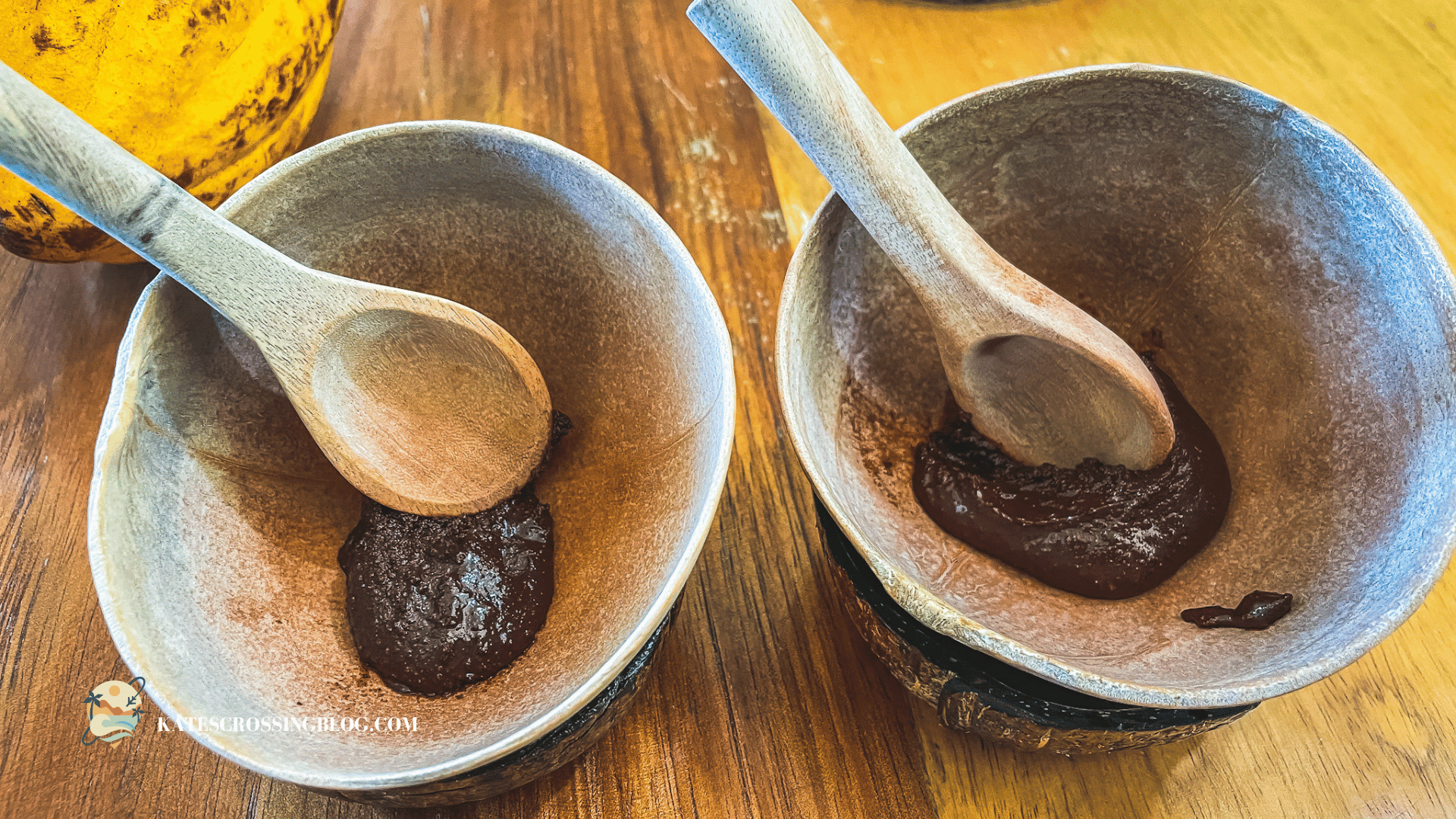Two bowls made out of coconut shells with fresh cacao paste and wooden spoons inside them. 