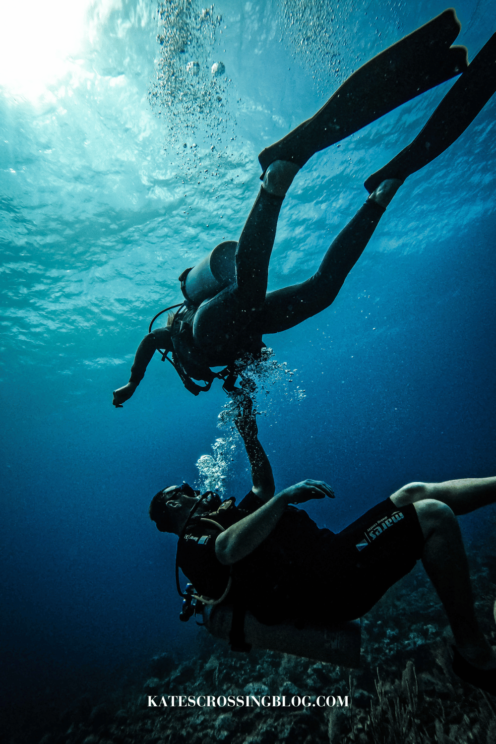 Kate and her husband scuba diving in Belize's crystal clear turquoise water, as her husband checks her oxygen levels. 