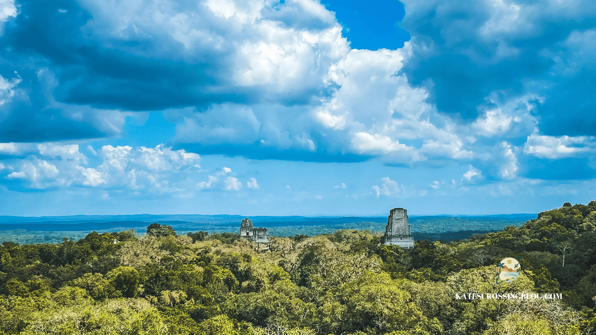 Jungle trees with the tops of two Mayan temples rising above the tree tops. 