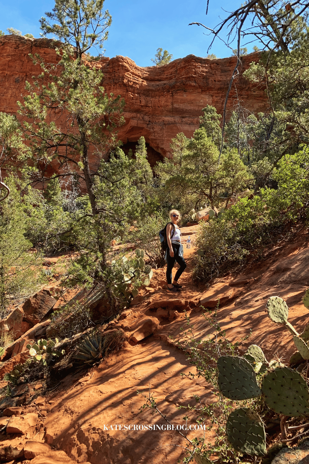 Kate hiking up the rocky trail surrounded by greenery and cacti, approaching the entrance to the hidden Soldier Pass Cave in Sedona.