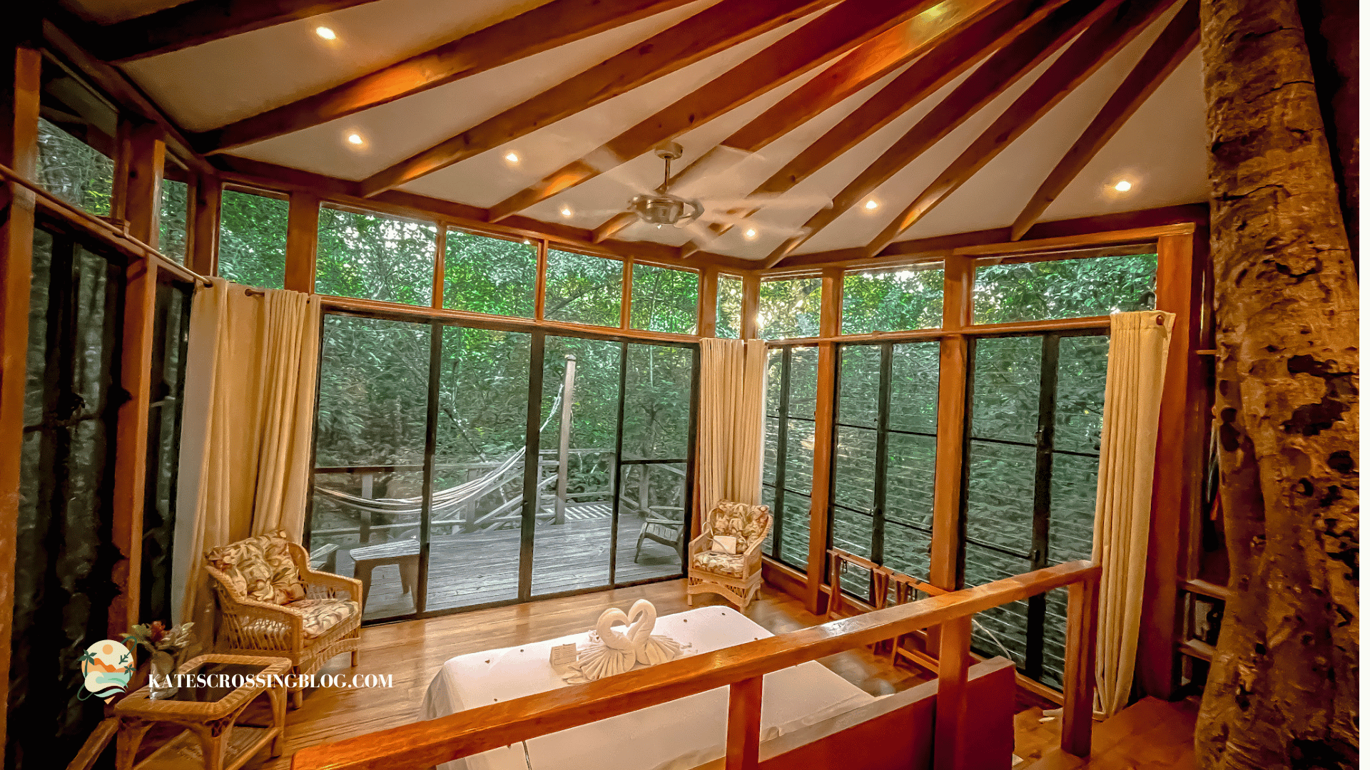 Bedroom with floor-to-ceiling windows inside a treehouse with a wood ceiling and jungle trees outside the windows. 