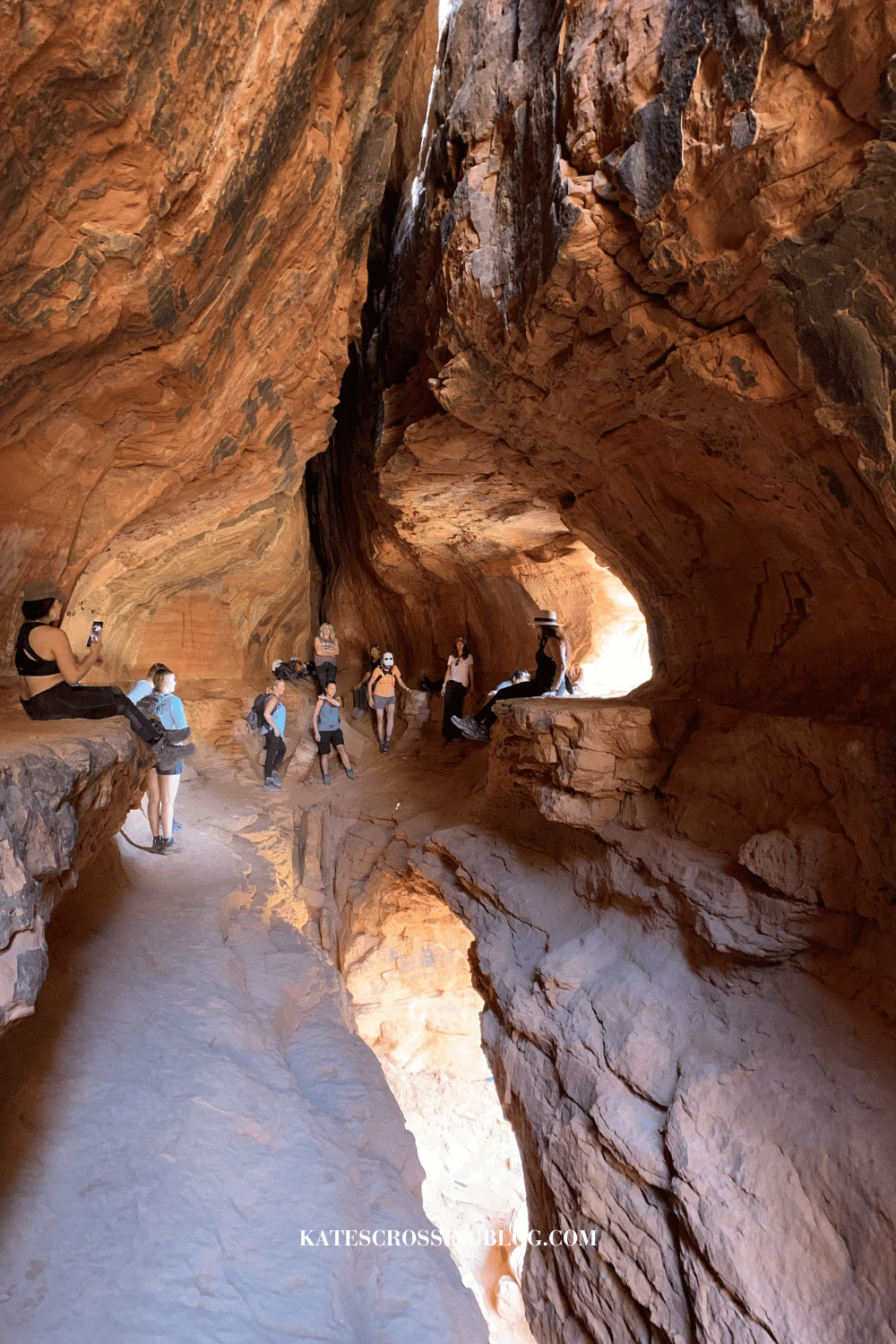 Hikers exploring the spacious interior of the hidden Soldier Pass Cave in Sedona, with its striking red rock formations and natural light streaming in.
