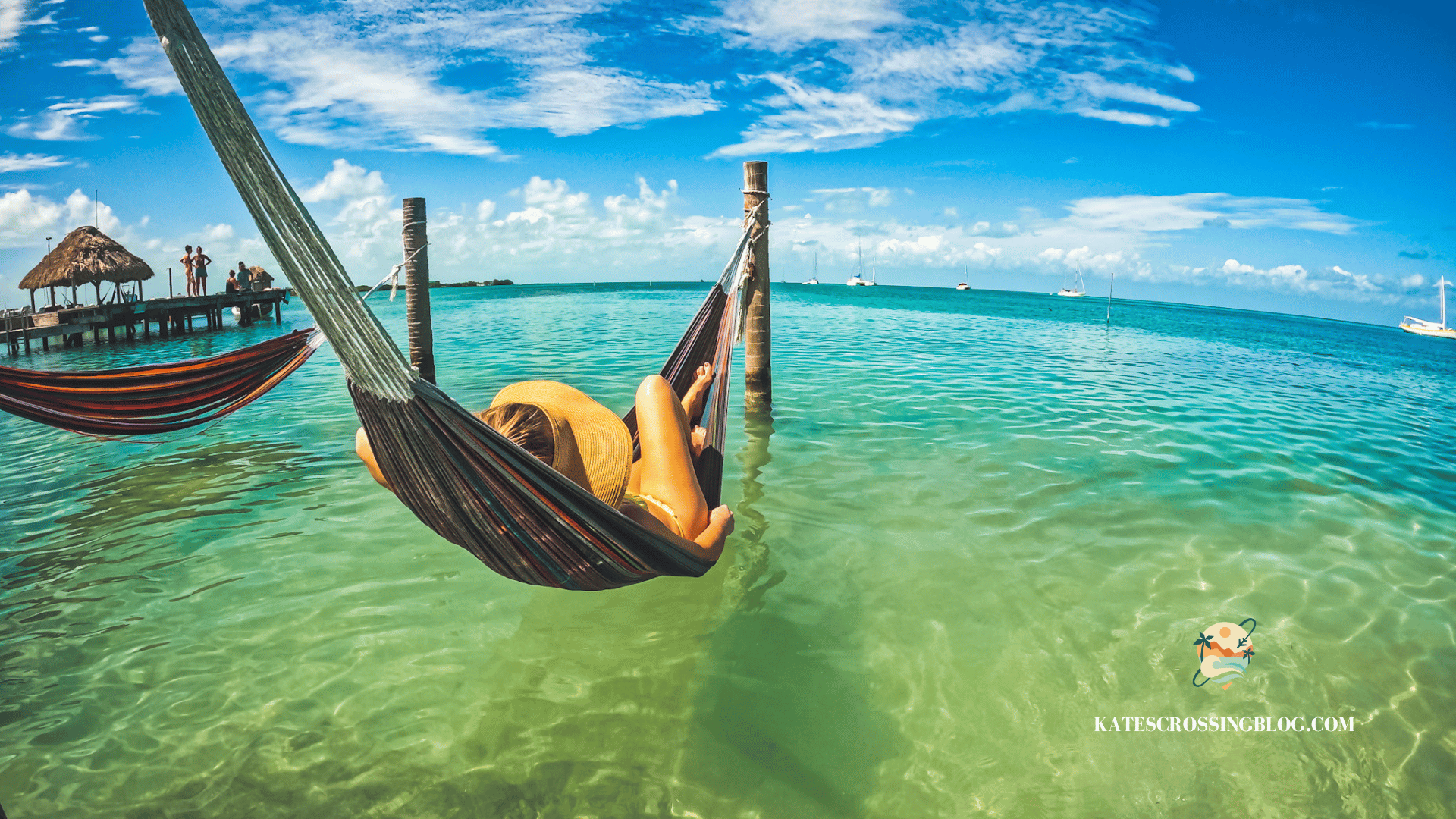 Kate is lying in an overwater hammock with sailboats and a dock in the distance. Featured as one of the Best things to do in Belize.