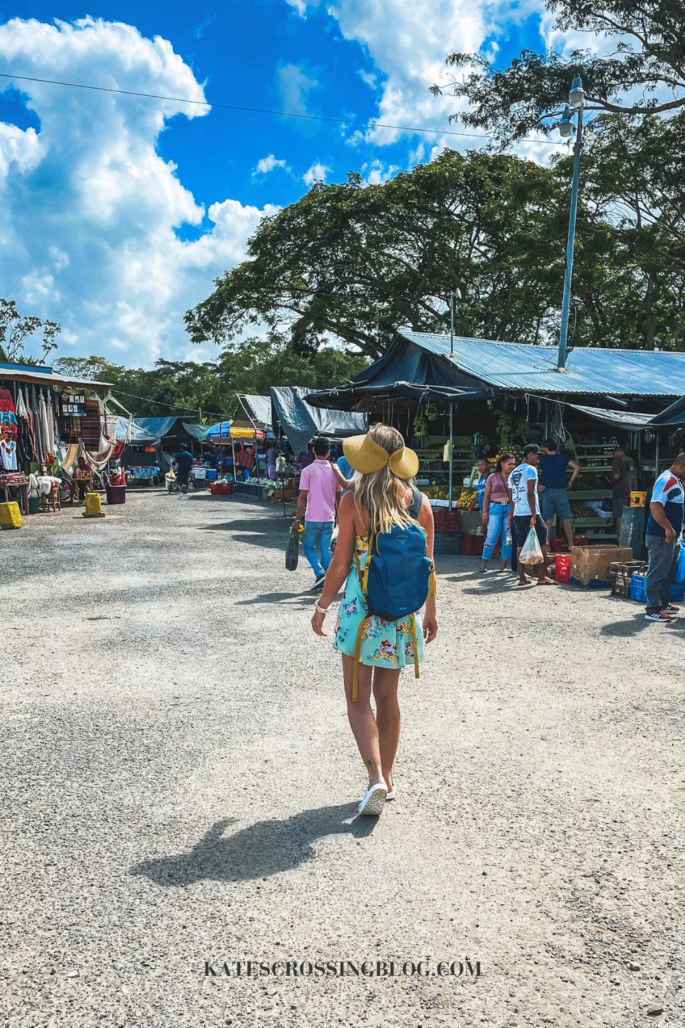 Kate walking between the stalls at the Farmers Market in San Ignacio Belize, wearing a floral sundress and sunhat. 