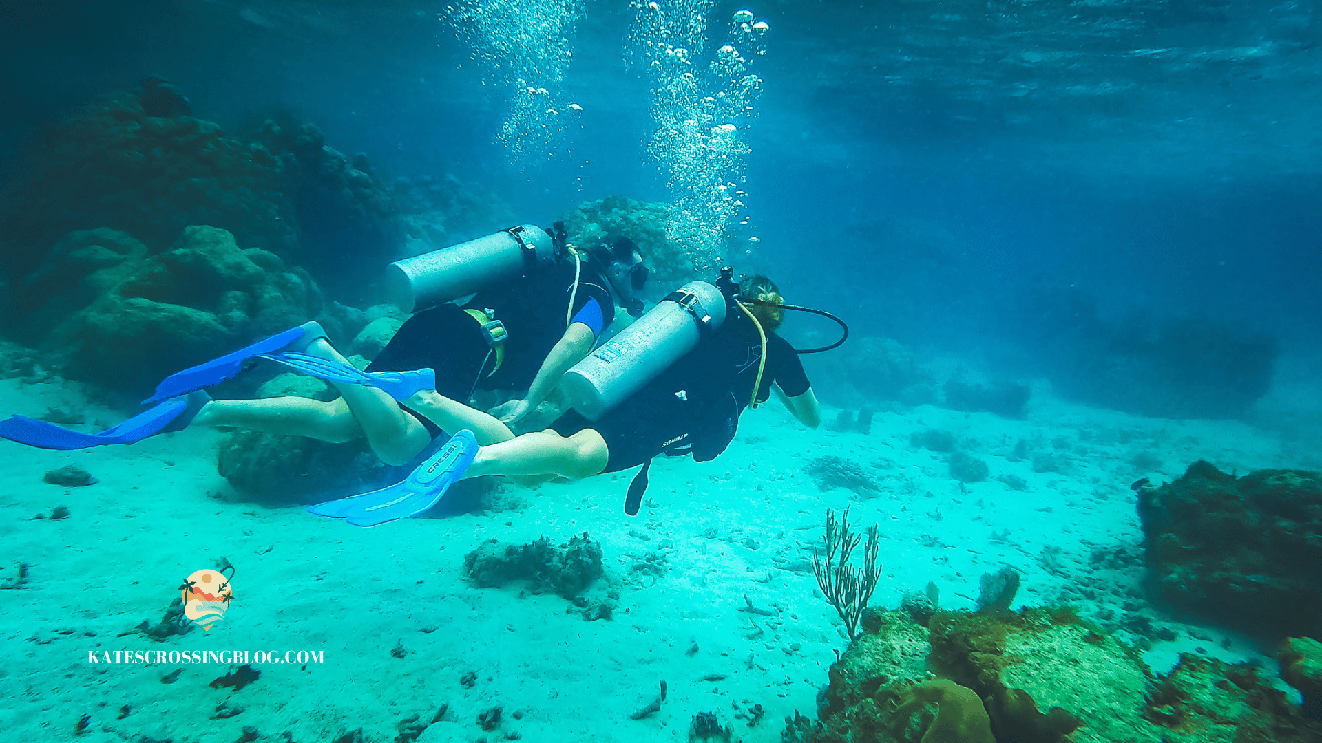 Kate and her husband scuba diving side by side under the turquoise waters of Belize with coral formations in the back ground. Featured as one of the best things to do in Belize. 