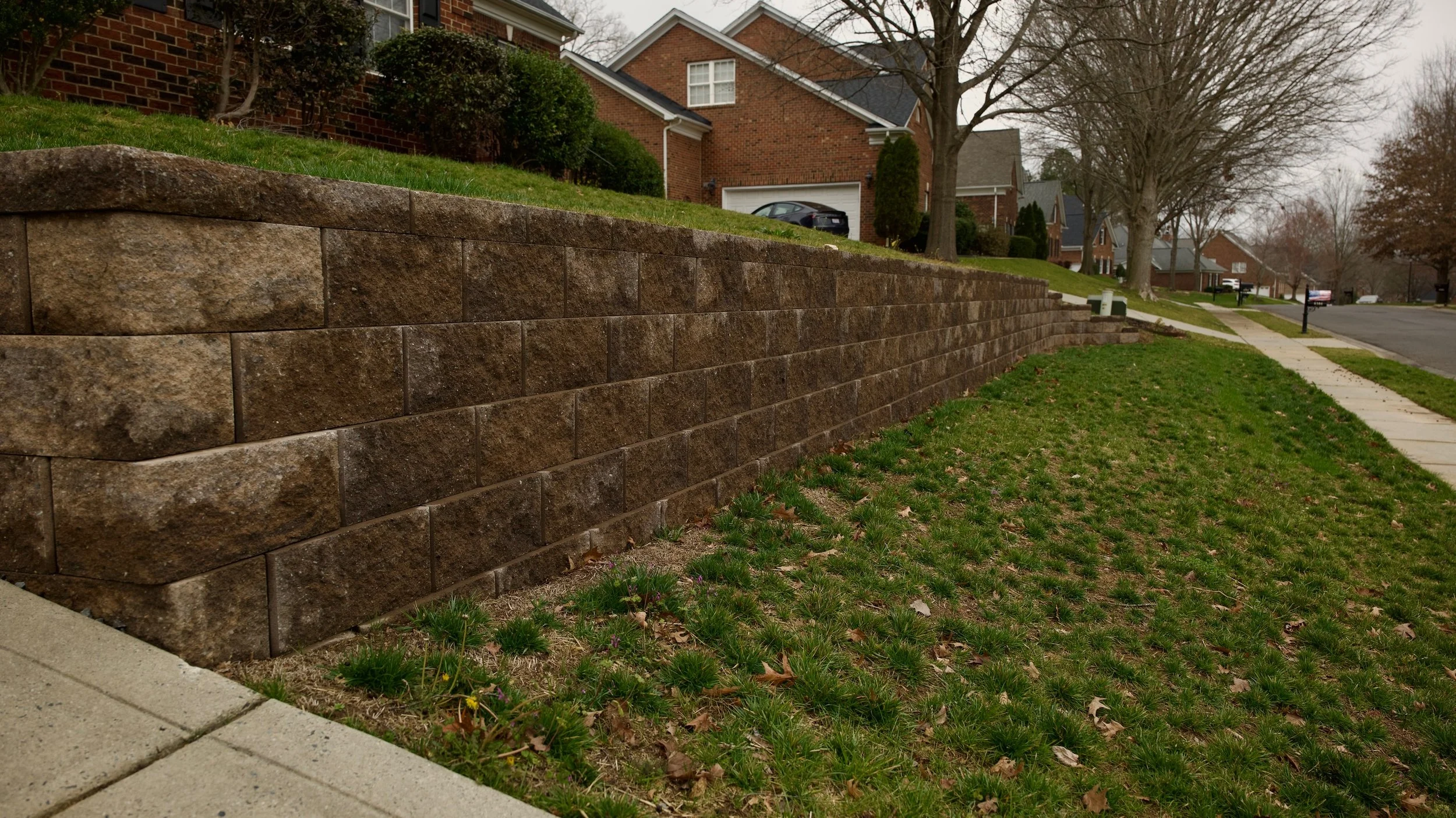 Lawn with a curved edge next to a tiered stone retaining wall, with plants and flowers on top of the wall.