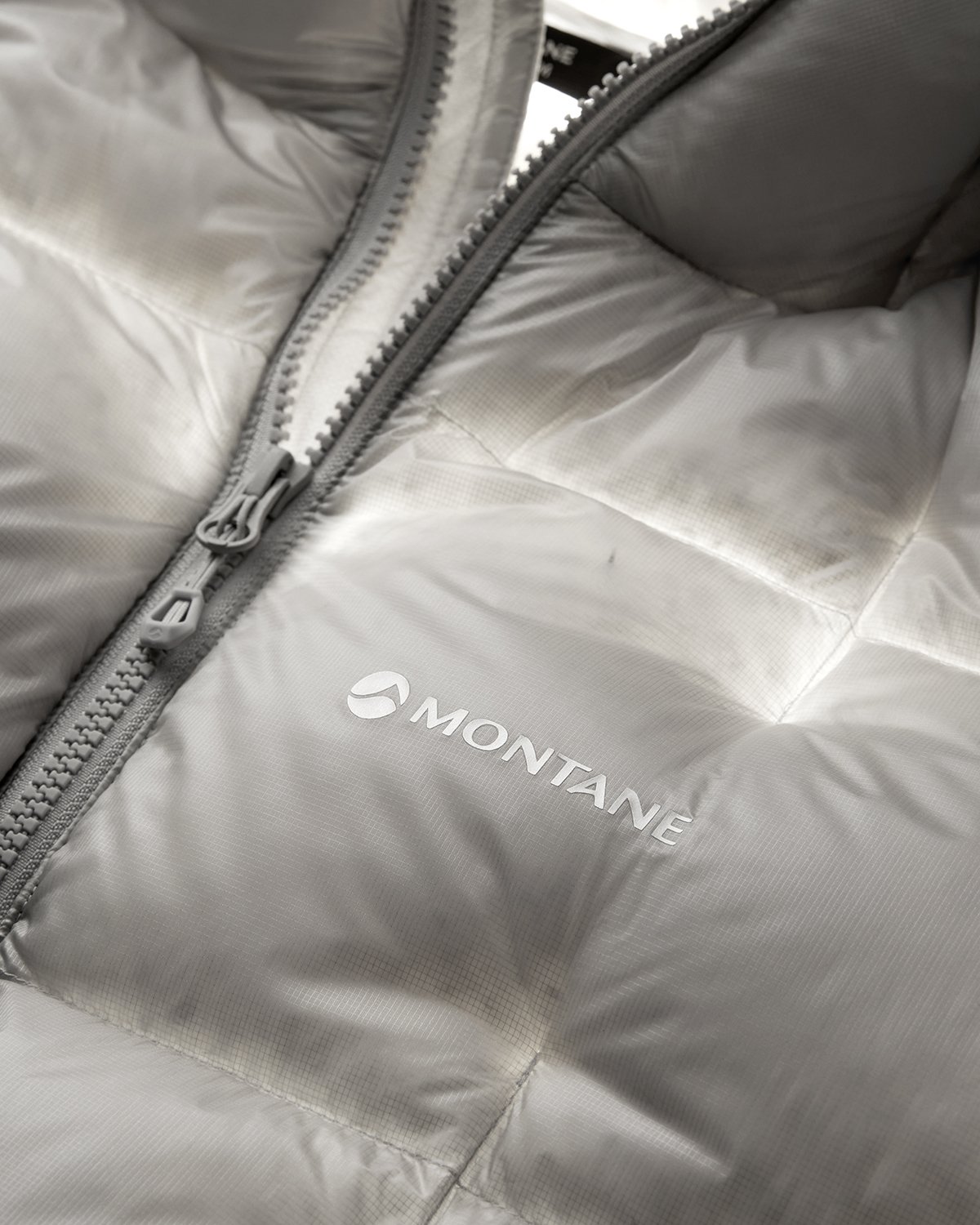 Close-up of a light gray Montane insulated jacket with a visible zipper and the Montane logo on the inside.