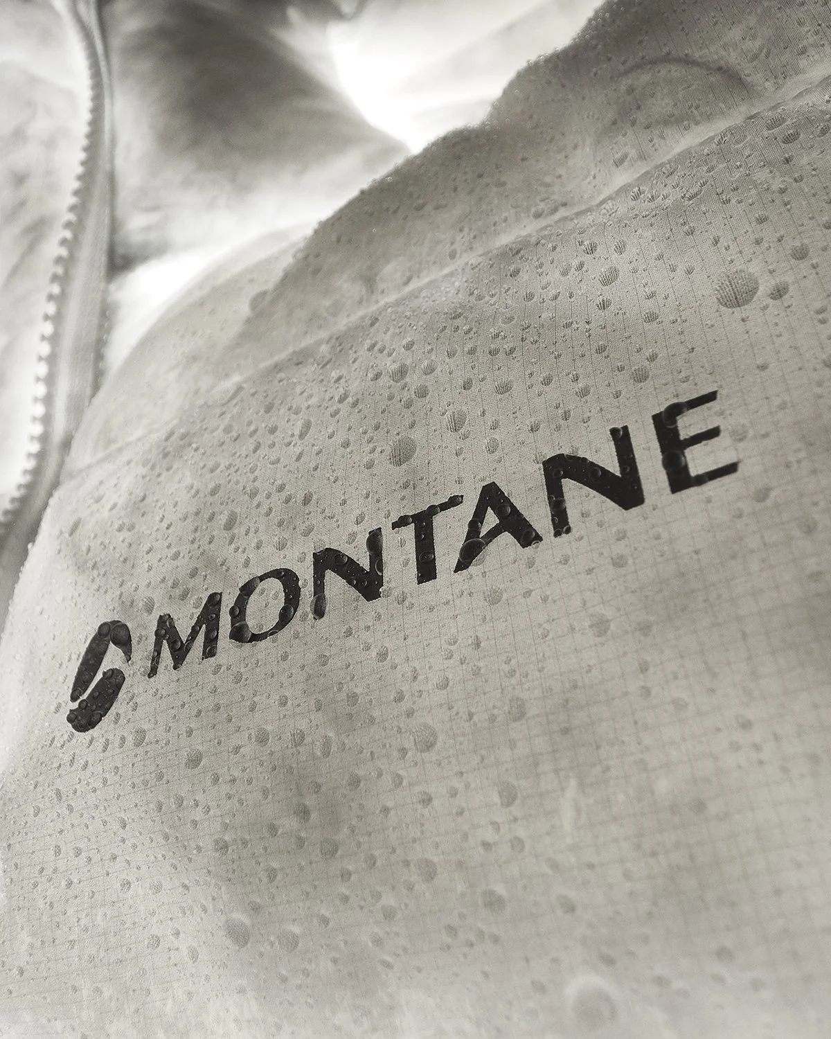 Close-up of a white Montane jacket with water droplets on the fabric, showing the brand name 'Montane'.