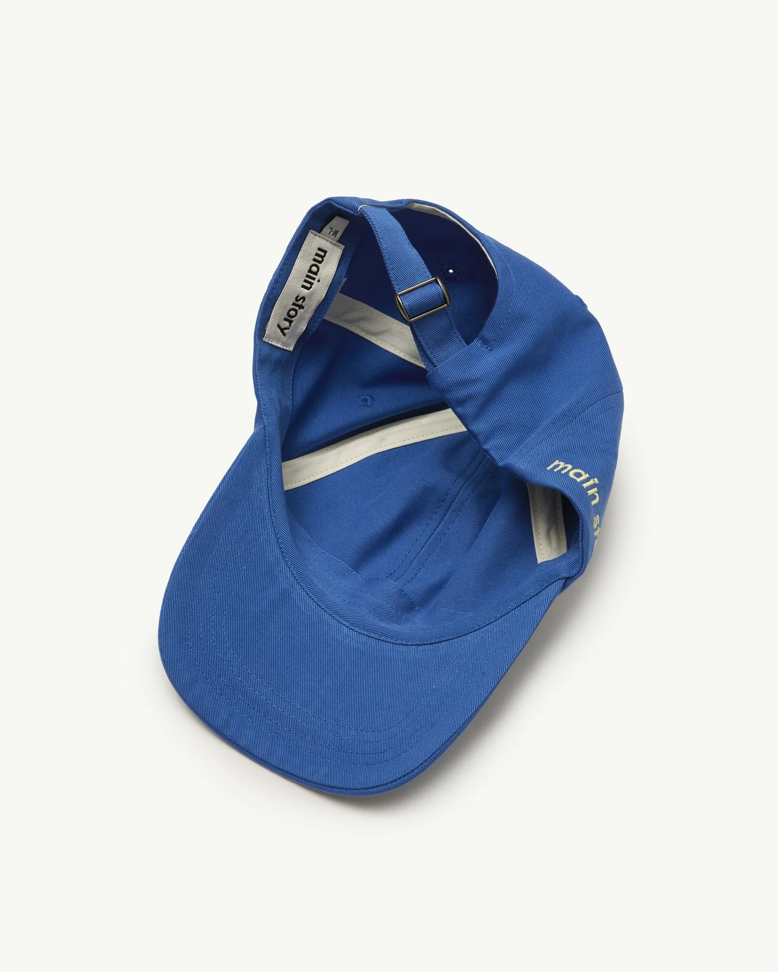 Blue baseball cap with adjustable strap inside, brand label 'main story' visible.