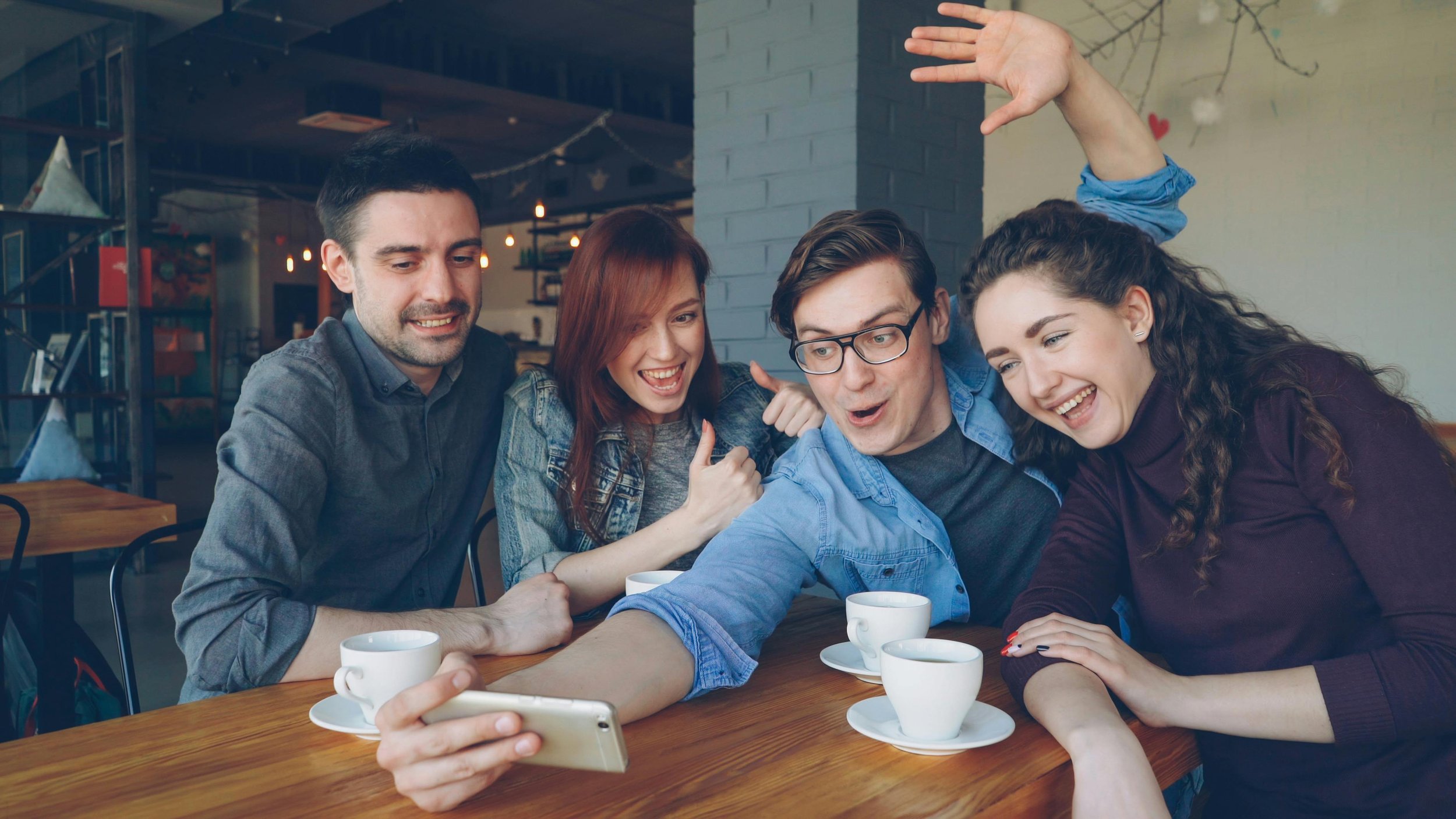 Four people at a coffee shop table taking a group selfie
